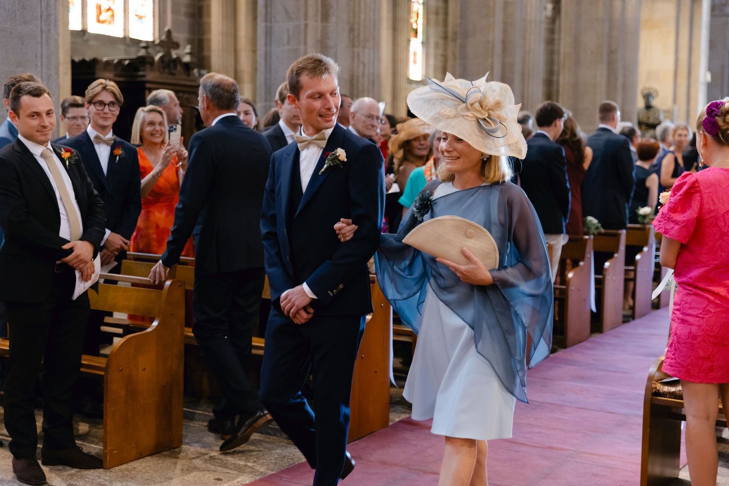 Cérémonie de mariage élégante dans une église avec un marié et des invités marchant dans l'allée en tenue formelle.