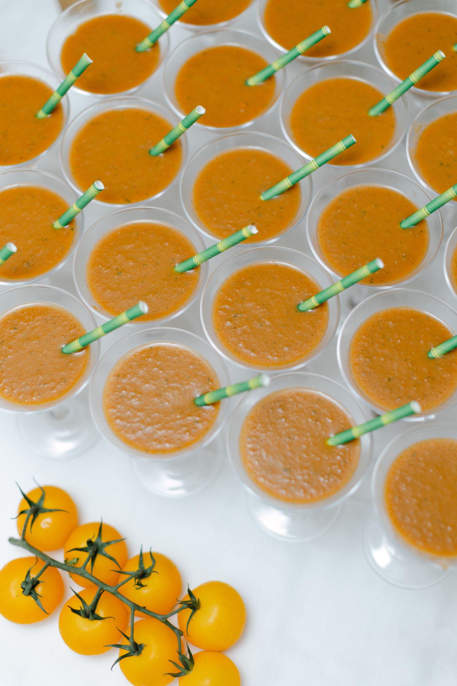 Des rangées de gaspacho avec des pailles en papier vert et des tomates cerises jaunes au cocktail de mariage.