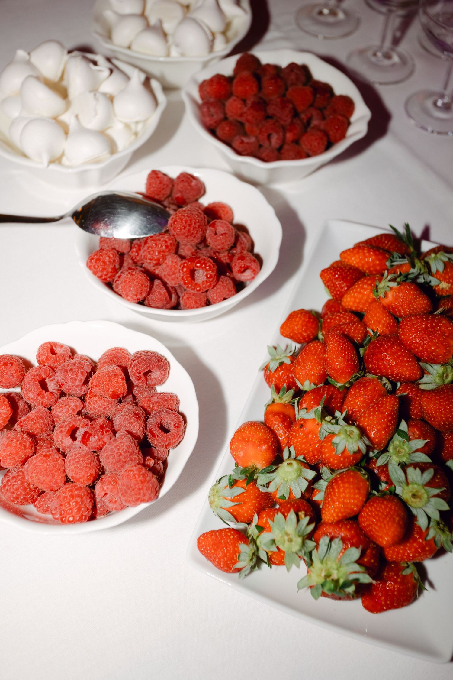 Table de desserts de mariage avec des fraises fraîches, des framboises et des meringues blanches disposées dans des assiettes blanches.