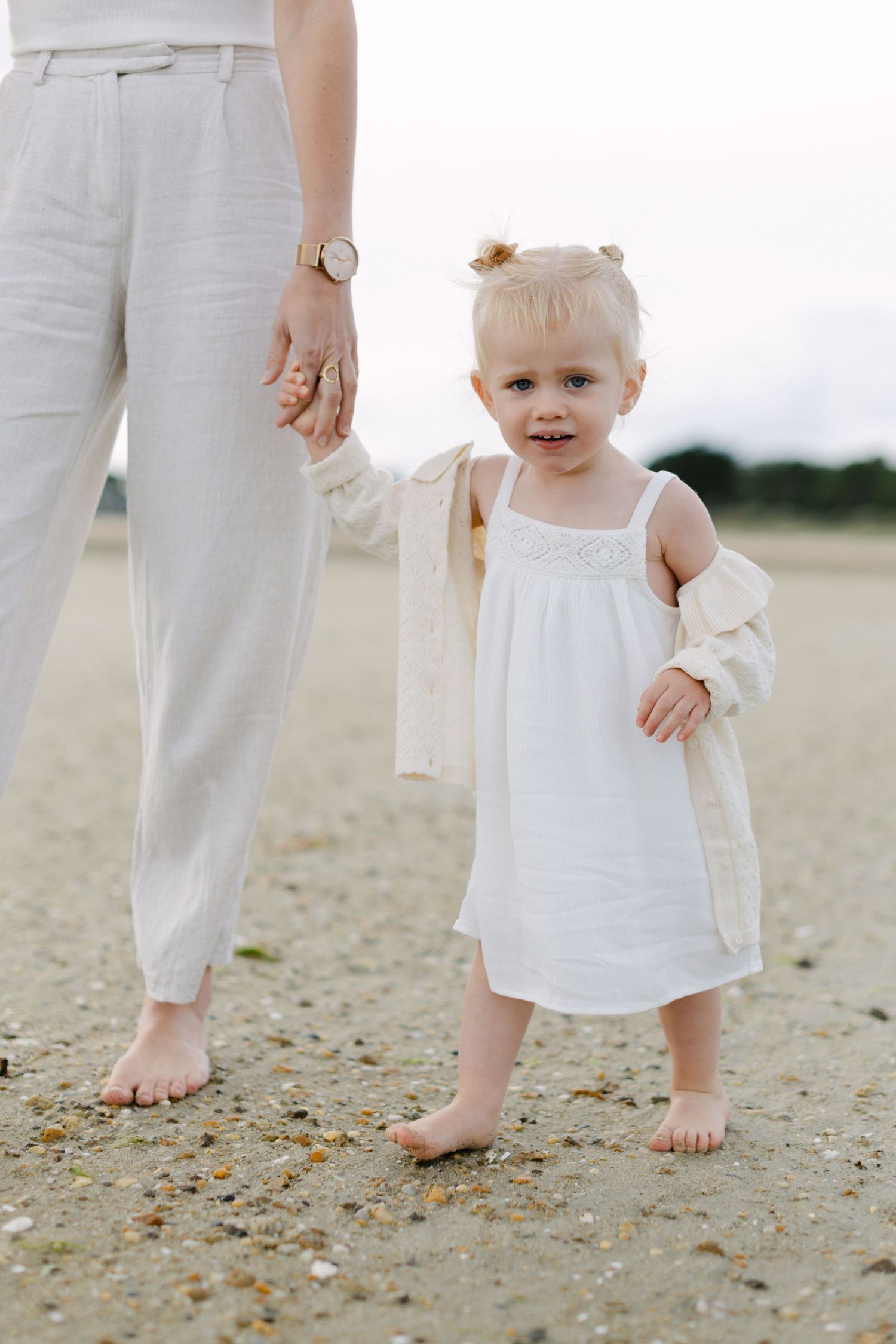 Adorable fille blonde en robe blanche tient la main de sa mère sur la plage de sable.