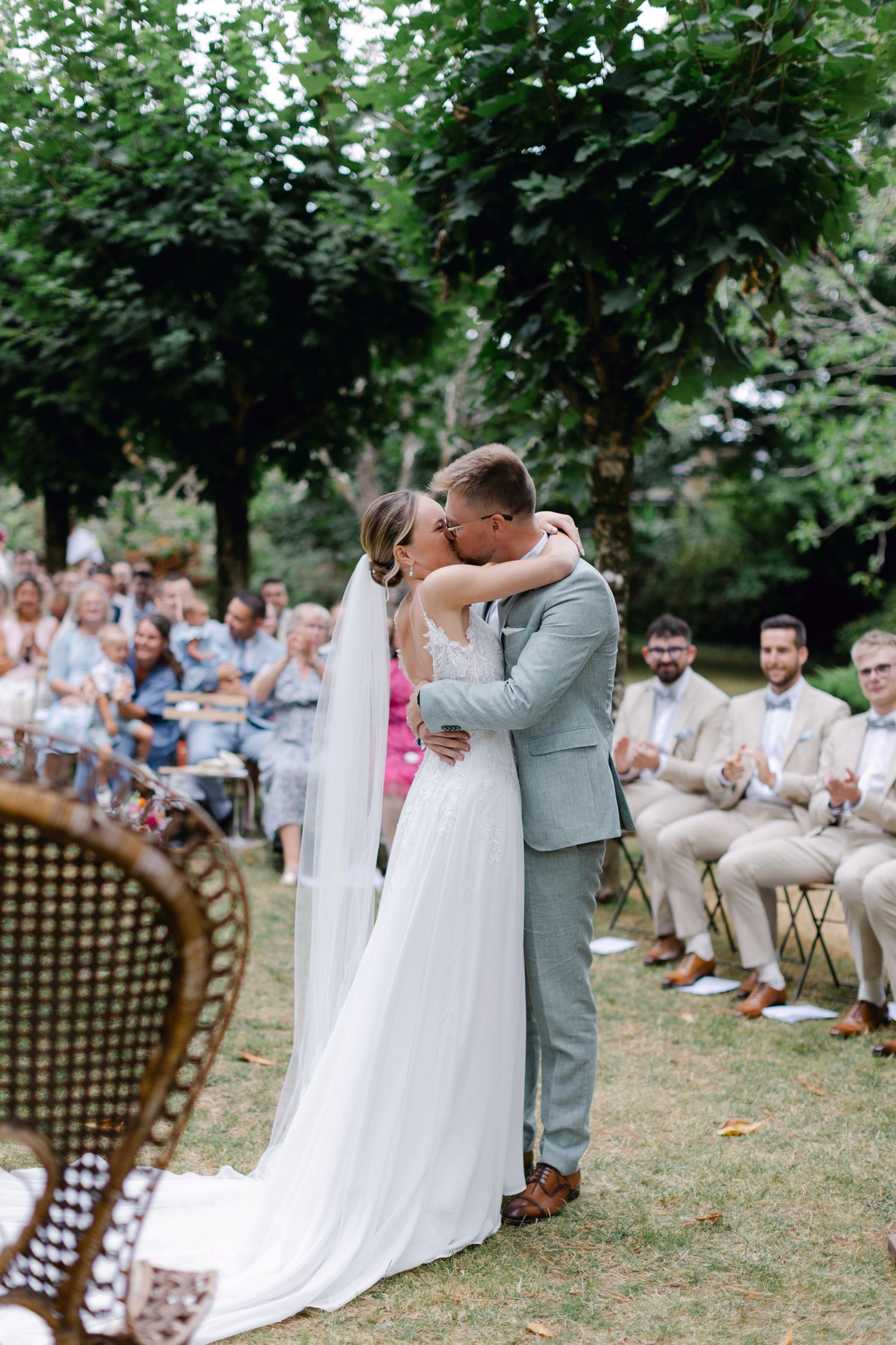 La mariée et le marié partagent le premier baiser lors de la cérémonie de mariage dans le jardin en plein air avec des invités assis.