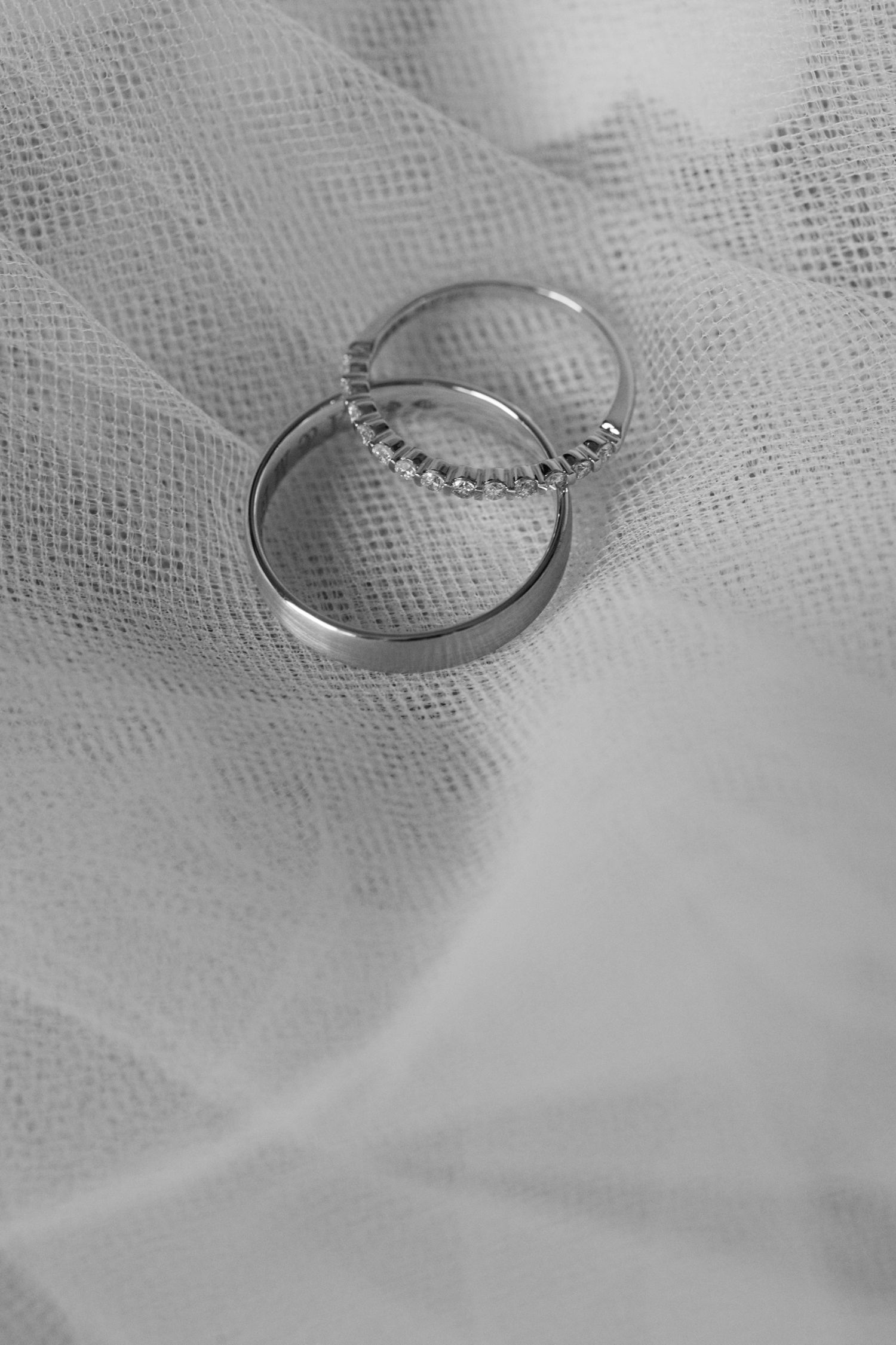 Deux alliances en argent, dont une incrustée de diamants, reposant sur un tissu de tulle blanc doux en noir et blanc.
