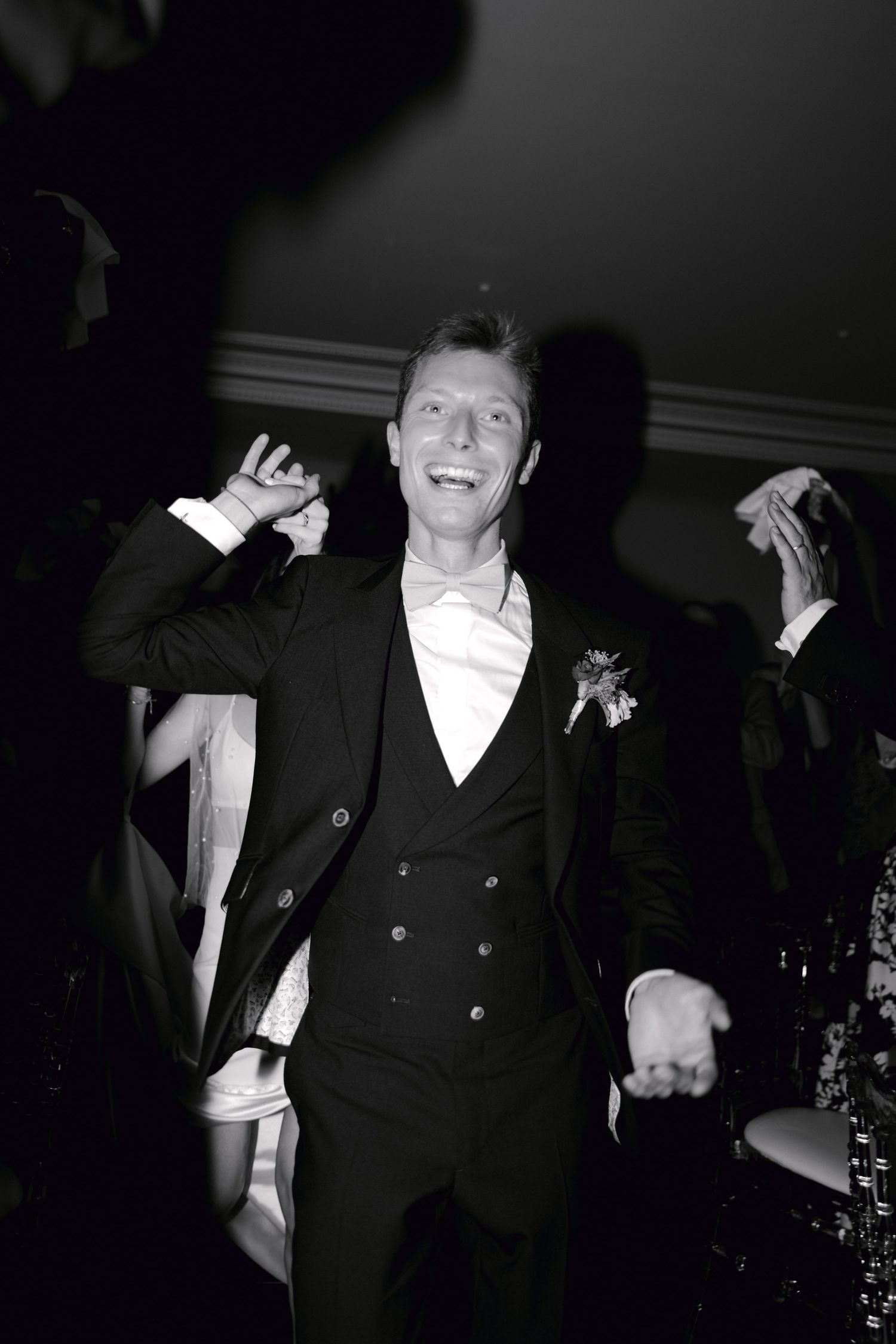 Un joyeux marié en smoking noir avec boutonnière danse lors d'une réception de mariage sur cette photo en noir et blanc.