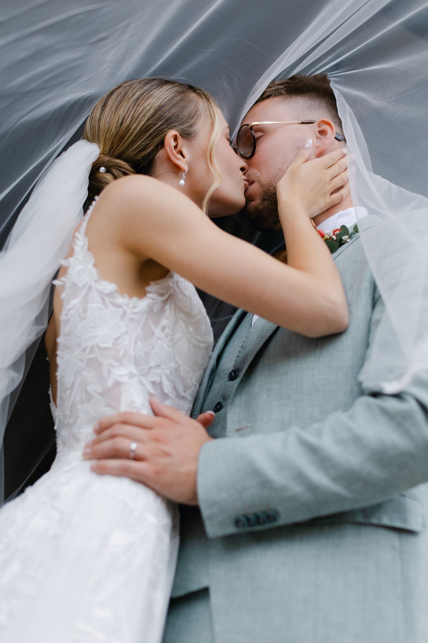 La mariée et le marié partagent un baiser passionné sous le voile de mariage dans un portrait intime au-dessus de la tête.