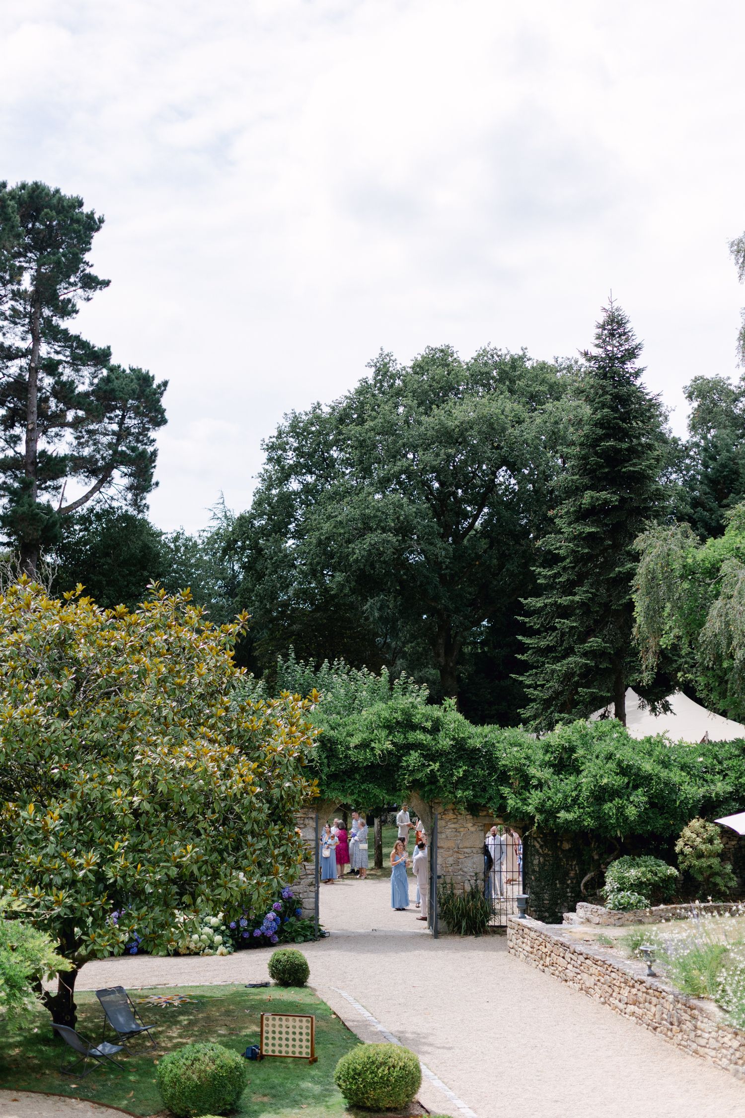 Chemin de jardin luxuriant avec de grands arbres et des invités en tenue colorée dans un élégant lieu de mariage en plein air.