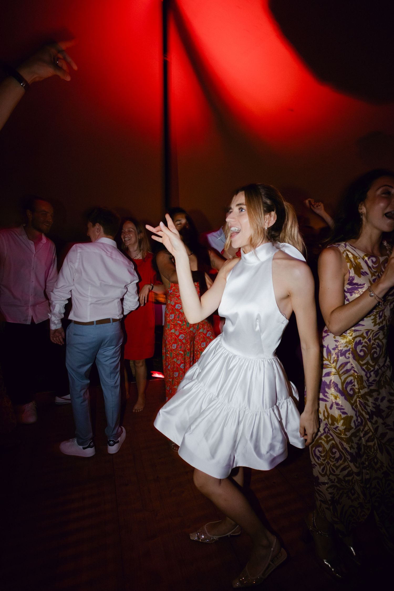 Femme en mini-robe licou en satin blanc dansant lors d'une réception de mariage animée.