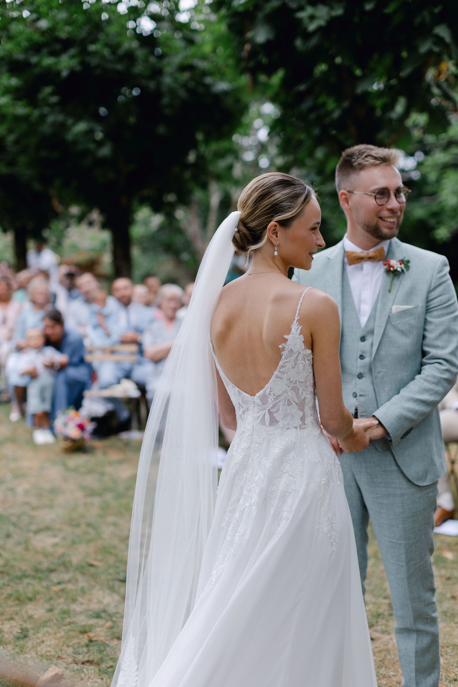 La mariée et le marié se tiennent ensemble face aux invités lors d'une cérémonie de mariage ensoleillée en plein air.