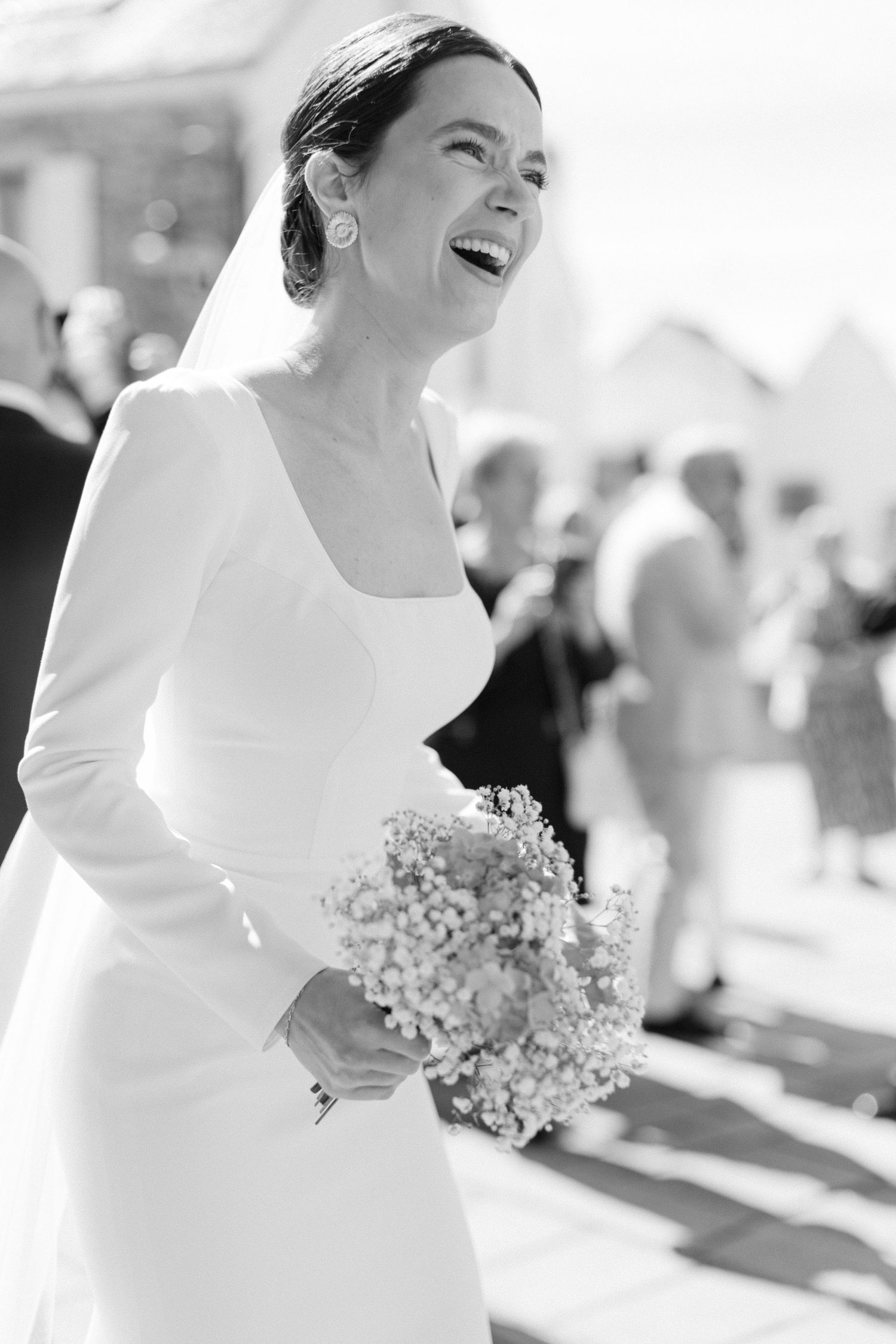 Portrait en noir et blanc d'une joyeuse mariée riant en robe blanche tenant un délicat bouquet floral.