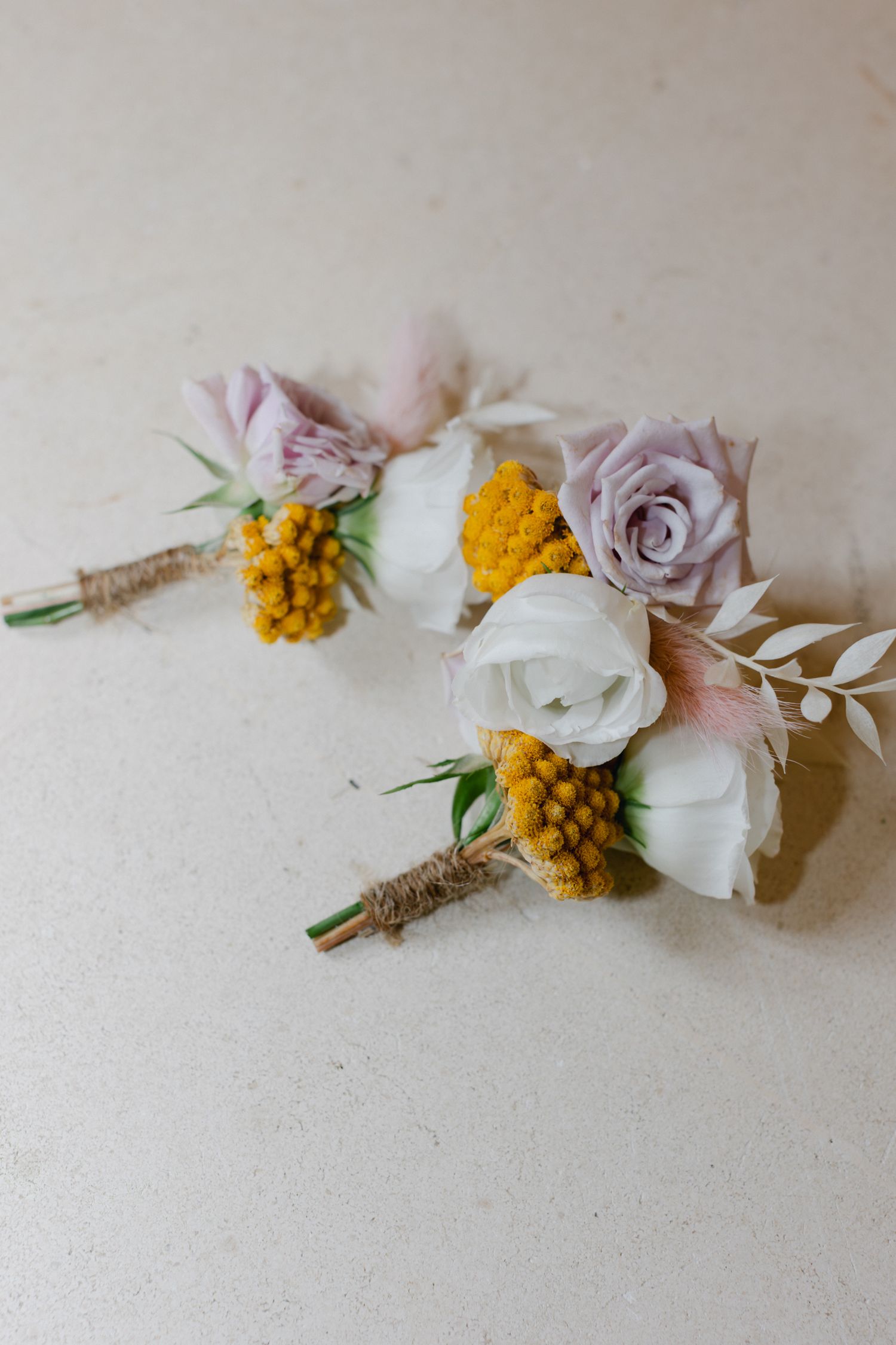 Deux élégantes boutonnières de mariage avec des roses blanches, des fleurs de lavande et des baies jaunes attachées avec de la ficelle.