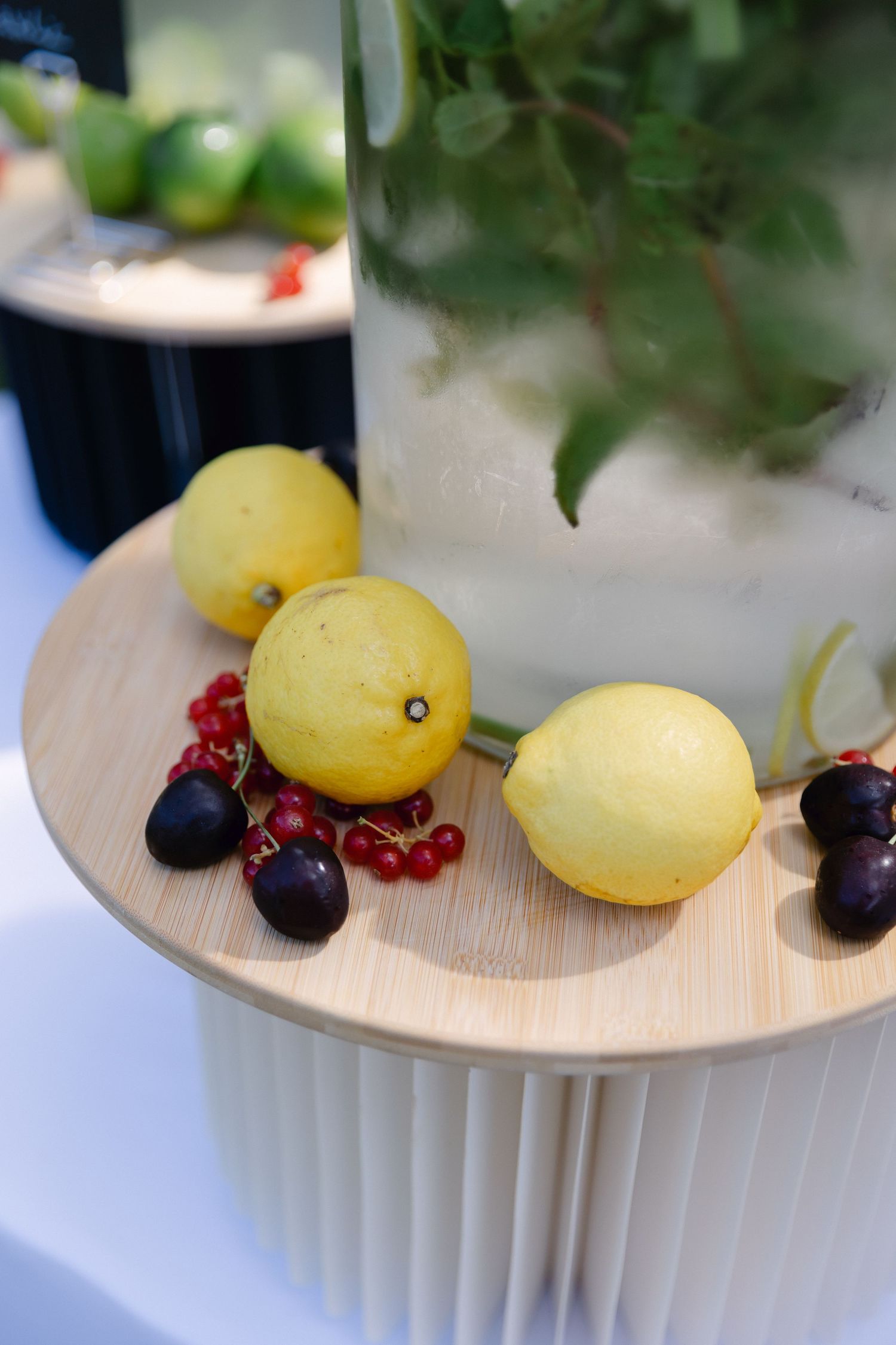 Citrons frais et groseilles rouges sur une planche de bois à côté d'un pichet en verre avec de la menthe et de la glace.