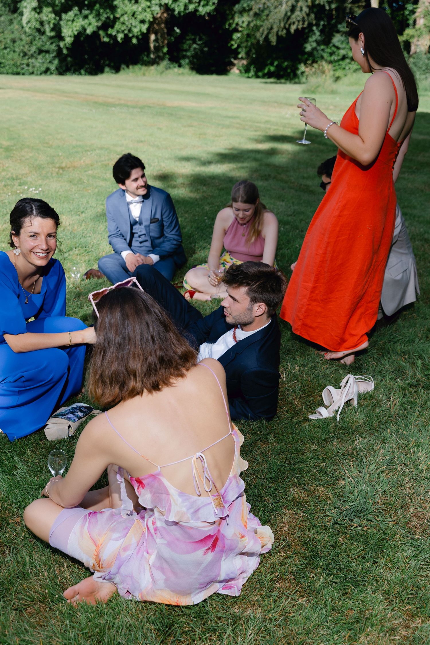 Groupe d'amis en tenue formelle colorée assis sur l'herbe verte lors d'une fête d'été en plein air dans le jardin.