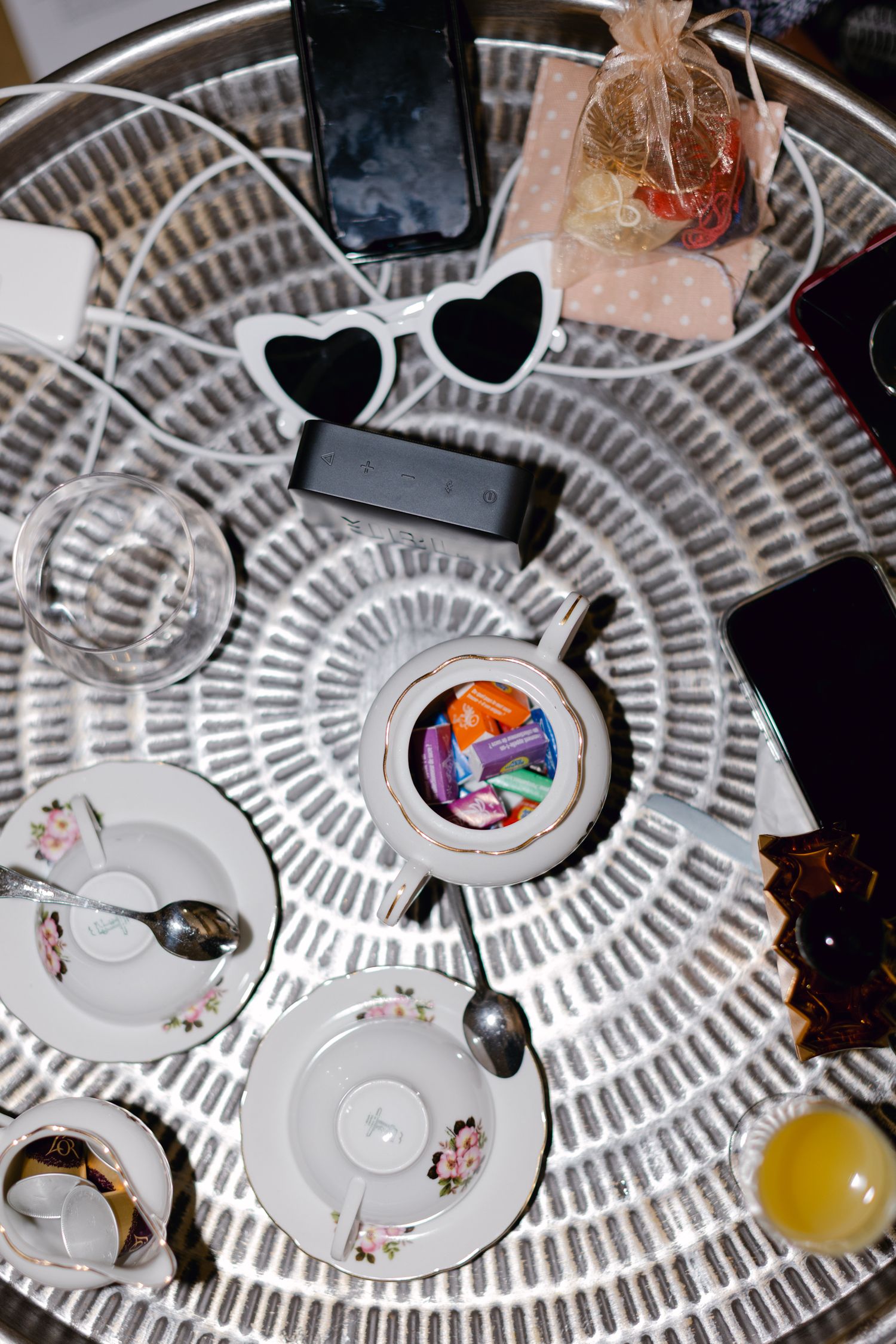 Vue aérienne d'un plateau décoratif avec des tasses à thé, des lunettes de soleil en forme de cœur, des téléphones et des bonbons colorés.