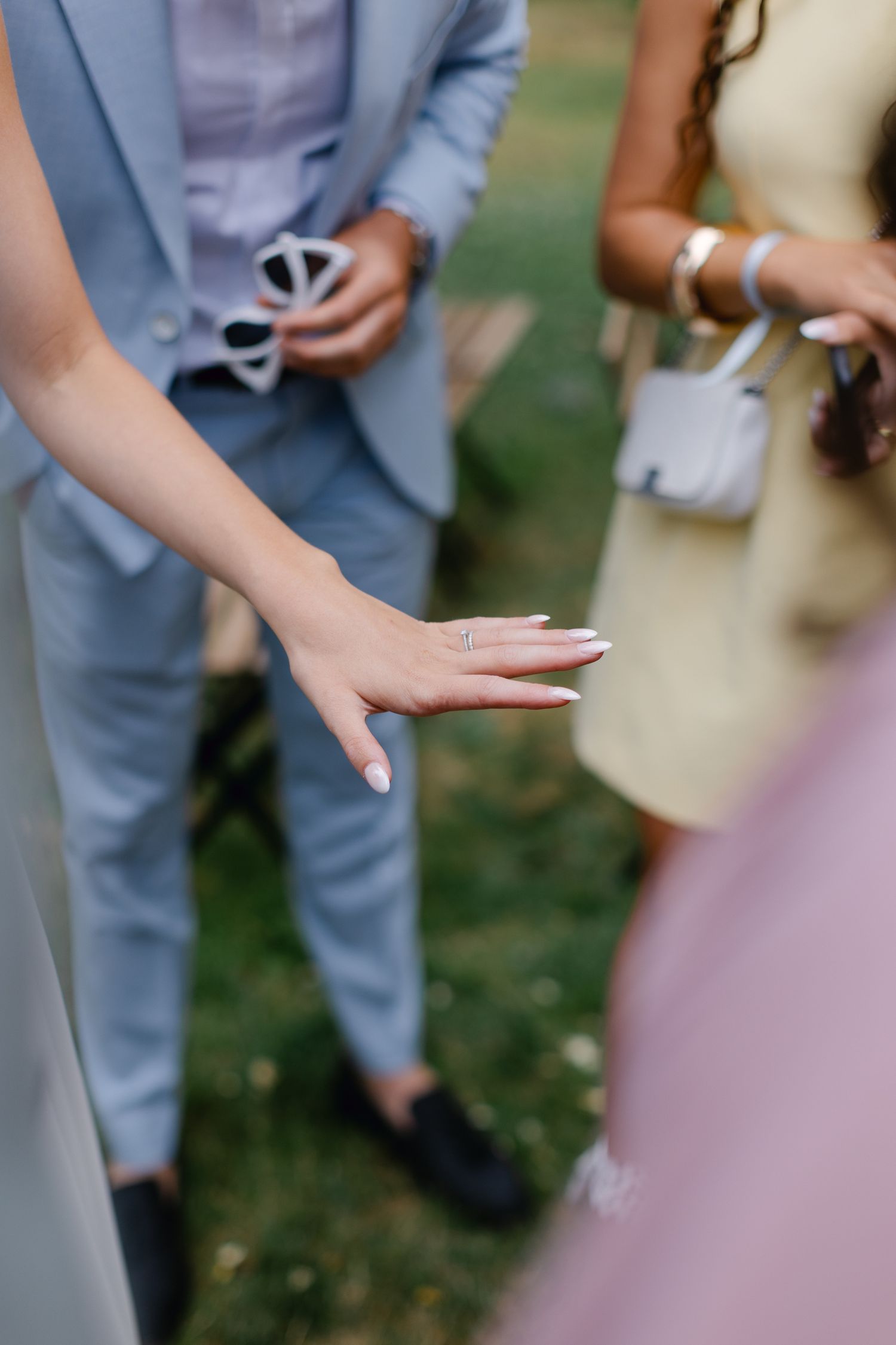 Gros plan de la main de la mariée affichant une nouvelle alliance pendant que les invités se mêlent à la réception en plein air.