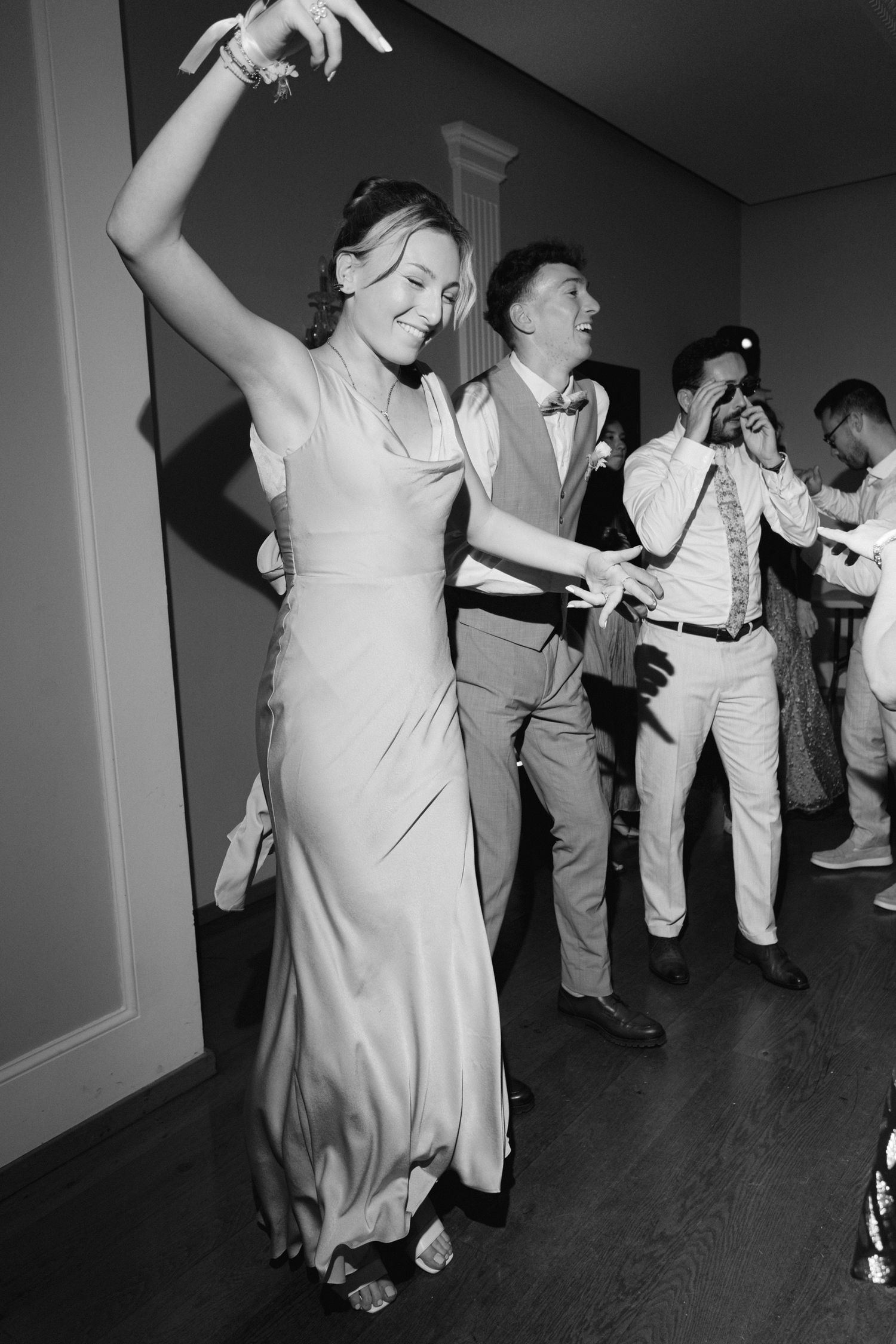 La demoiselle d'honneur en robe élégante danse joyeusement lors de la réception de mariage en photo en noir et blanc.
