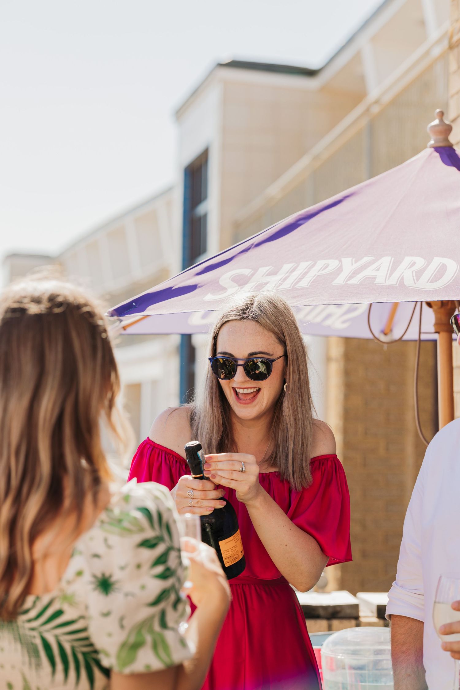 Guest in red dress laughing while holding drink under purple umbrella.