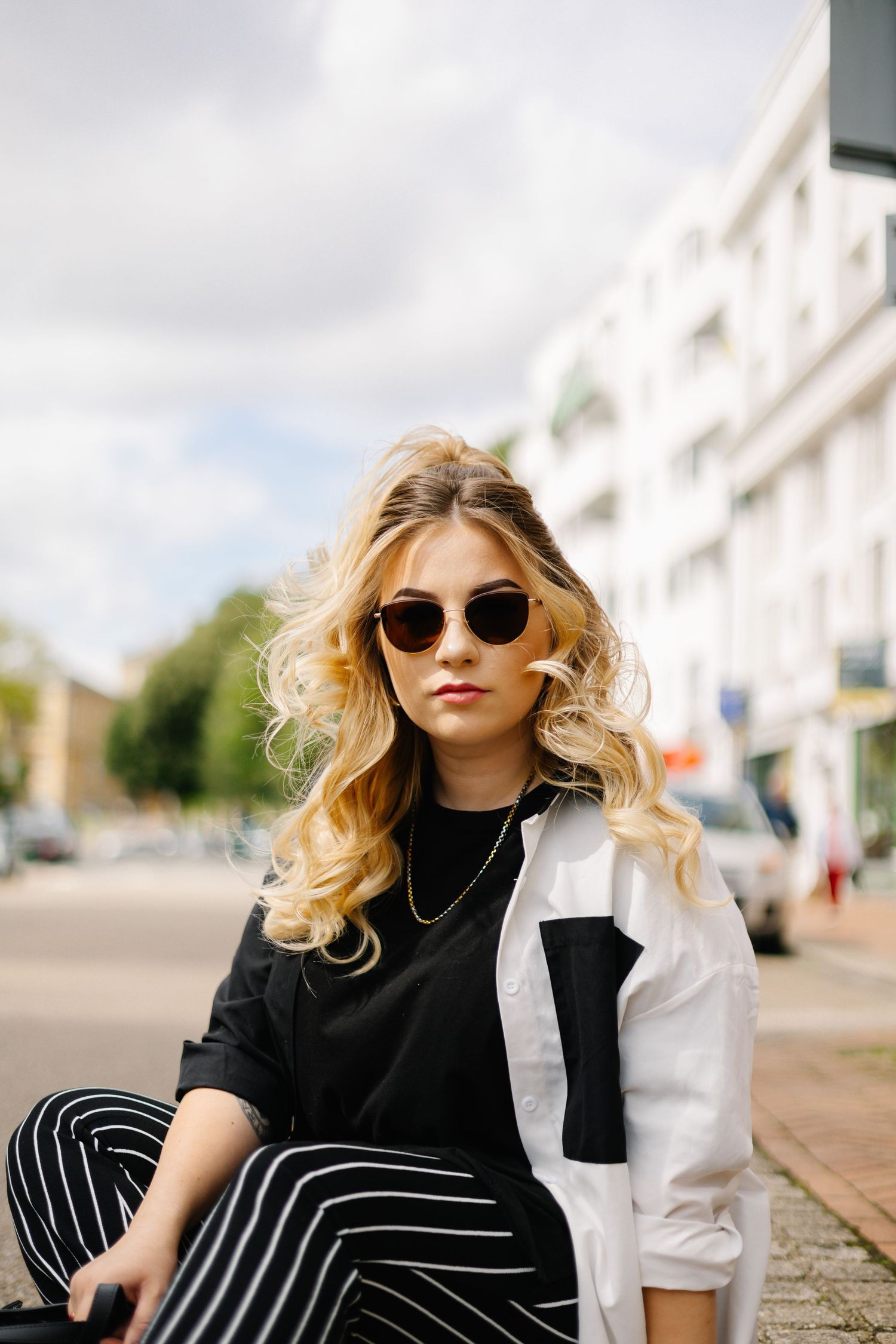 Fashion portrait of blonde woman in black and white outfit with sunglasses on city street.