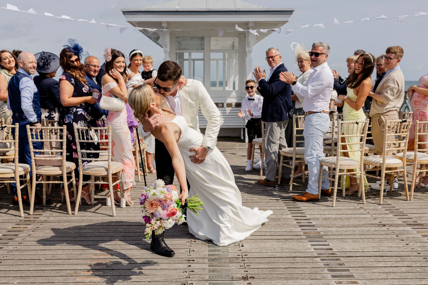 A dramatic dip kiss during an outdoor wedding ceremony with guests watching and applauding.