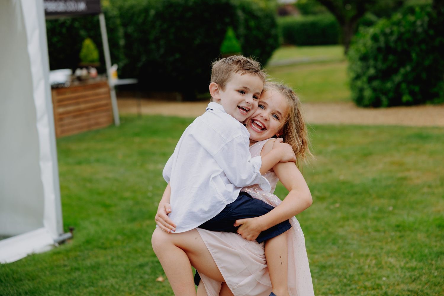 Two young children playing and laughing together on a lawn during a wedding celebration.