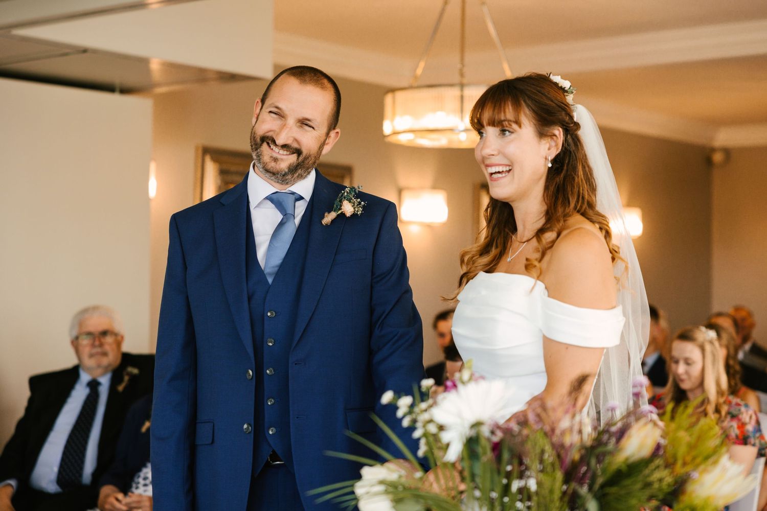 A joyful indoor wedding ceremony scene with warm lighting and floral decorations.