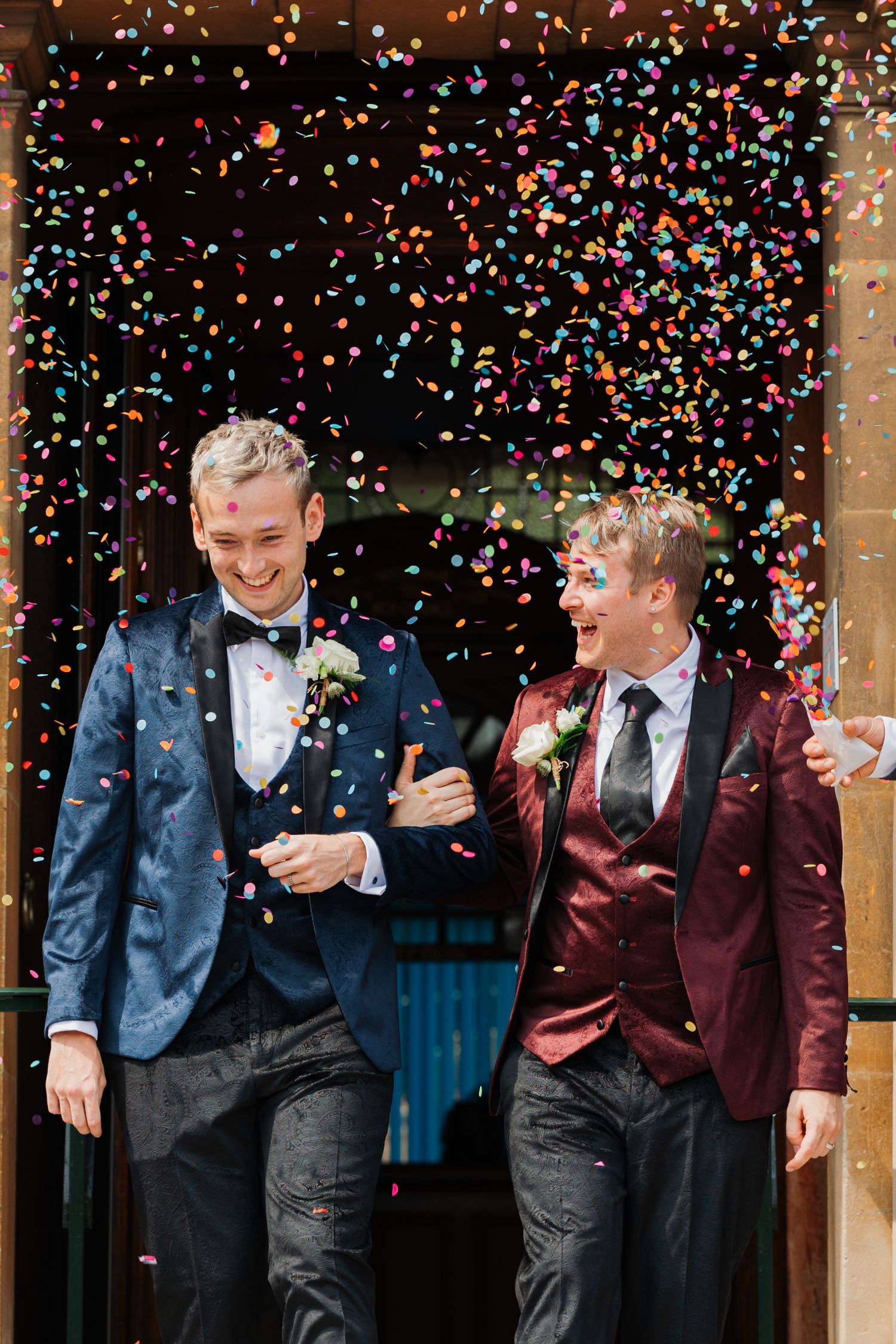 Two people celebrating with joy as colorful confetti rains down around them at a wedding ceremony.