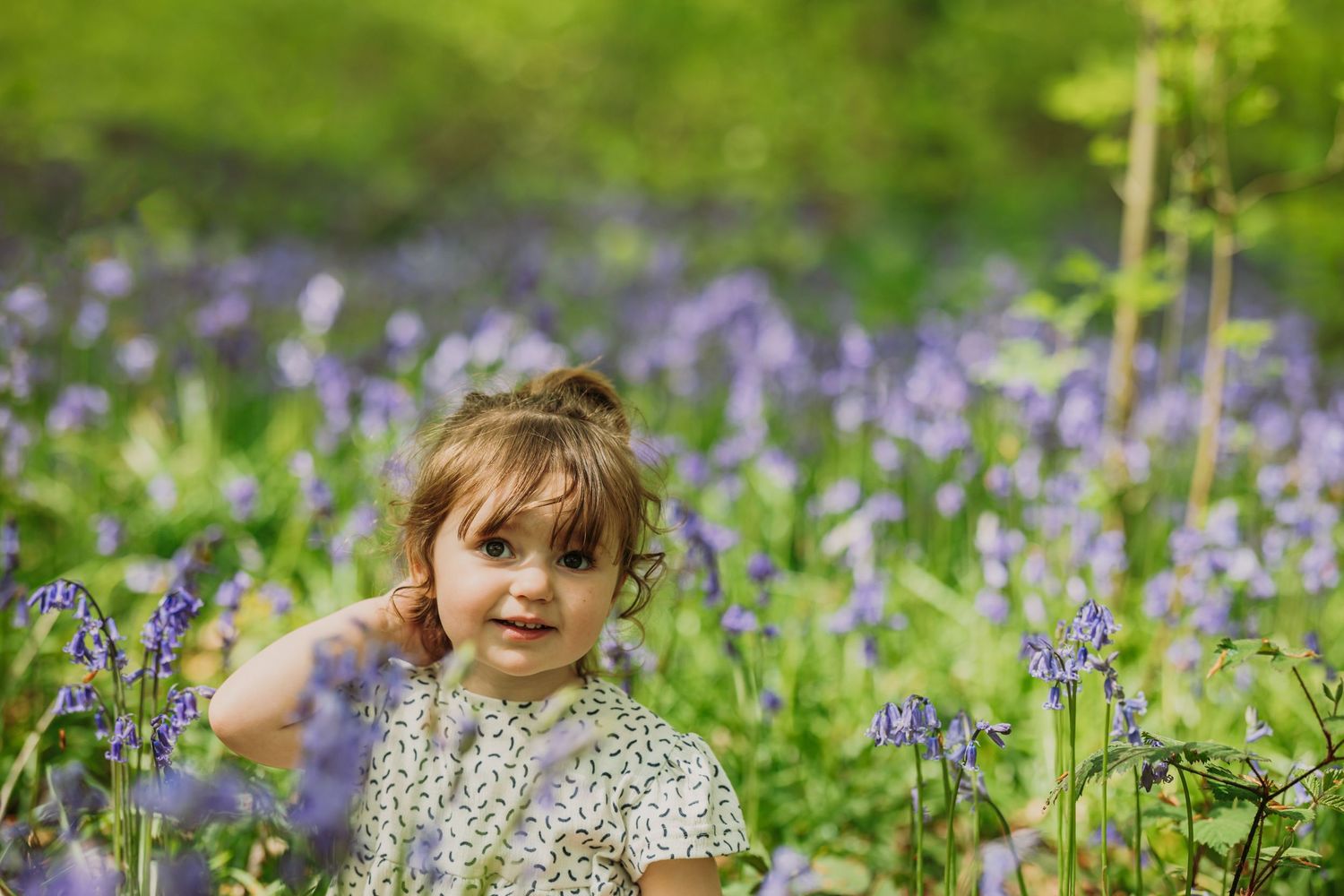 Young child sitting among purple bluebells in springtime woodland.