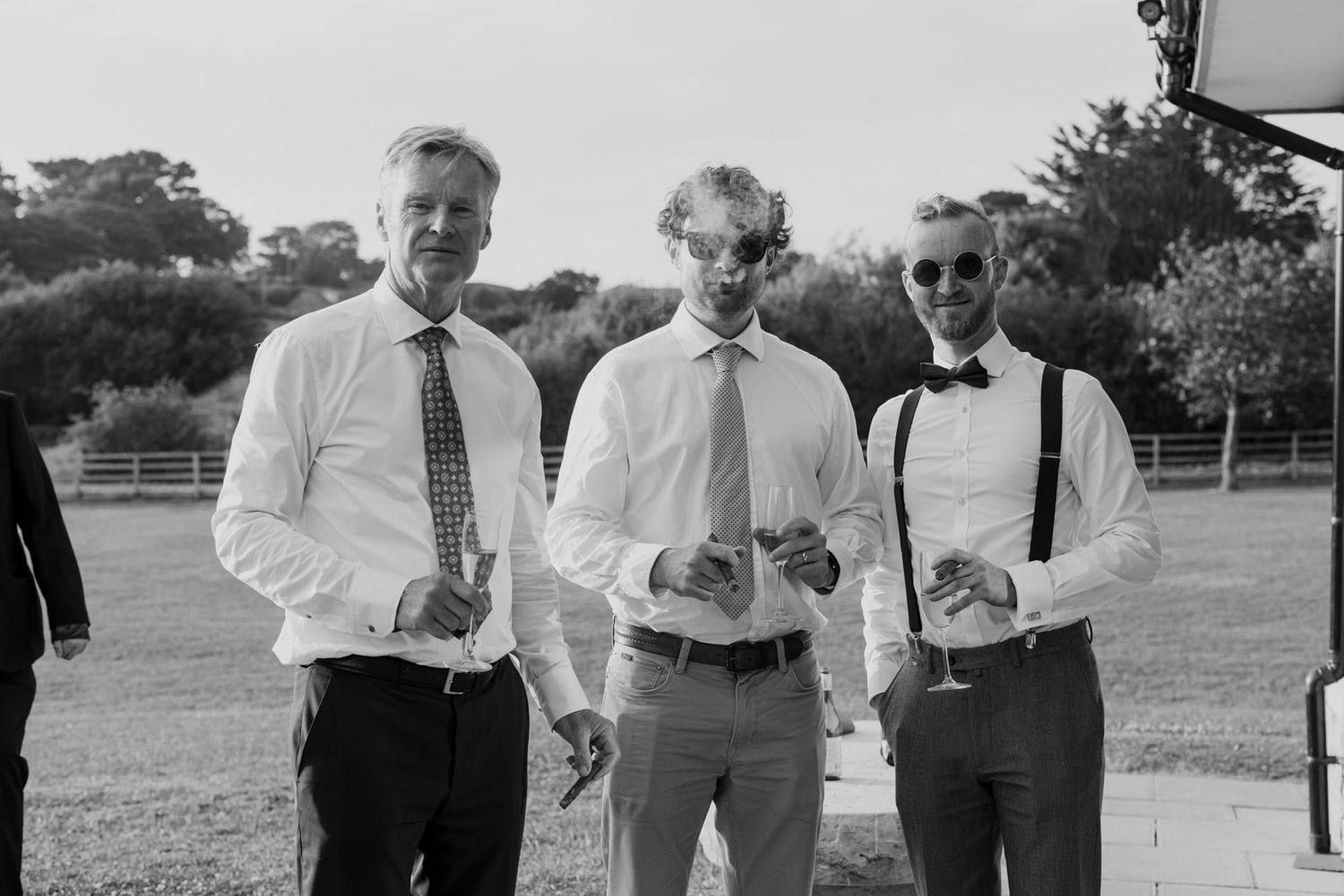 Three guests in formal attire enjoying drinks at an outdoor wedding reception.