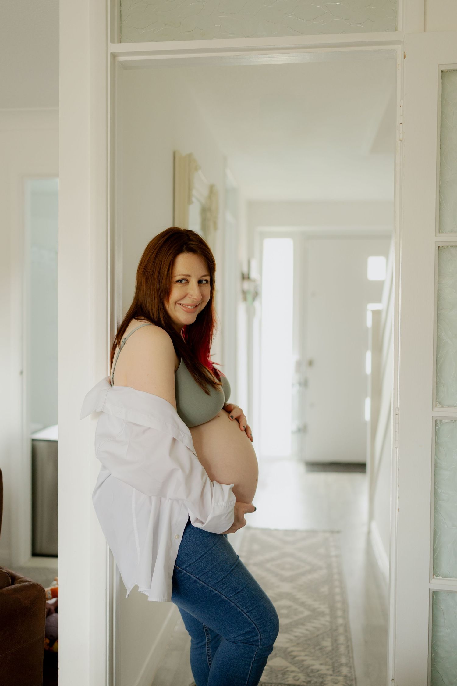 A person in a white shirt and denim overalls leans against a bright interior wall in a home.