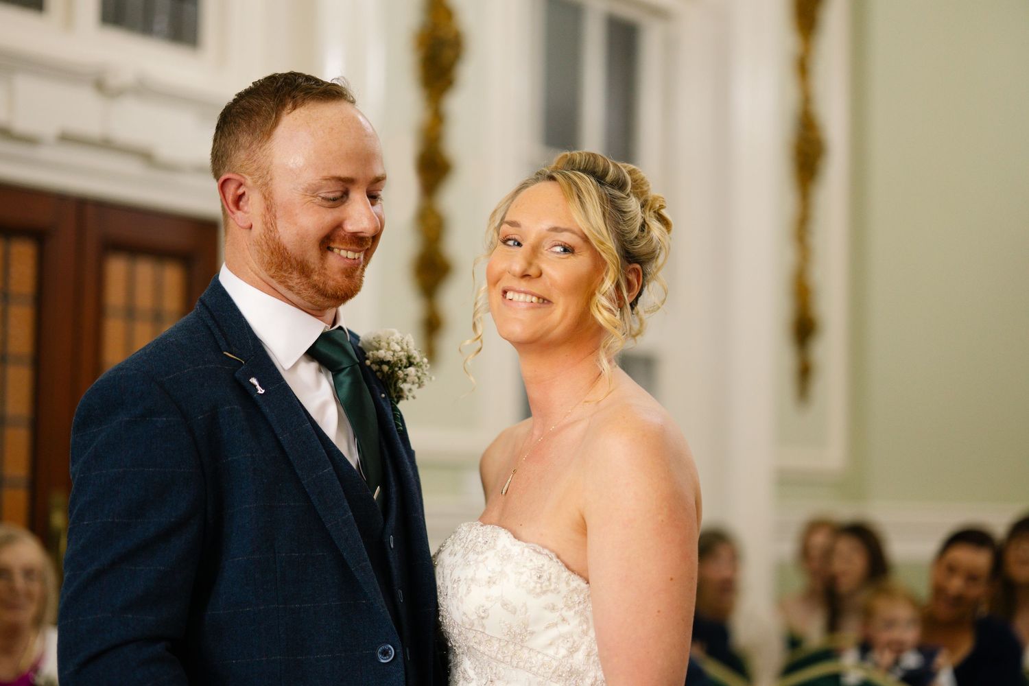A joyful couple shares a tender moment during their wedding ceremony in an elegant church with white pillars.