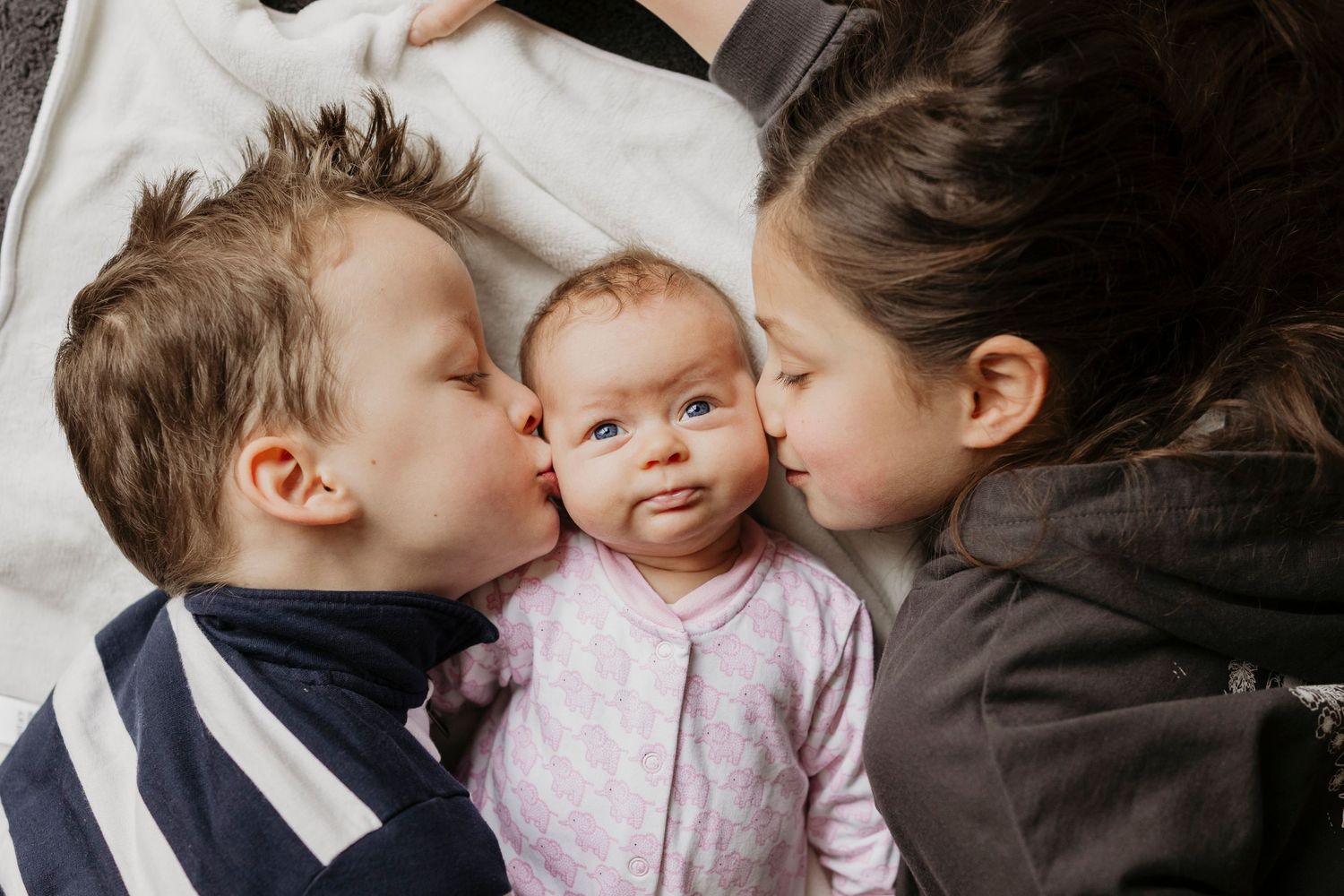 Two children kissing a baby's cheeks in an intimate family moment.