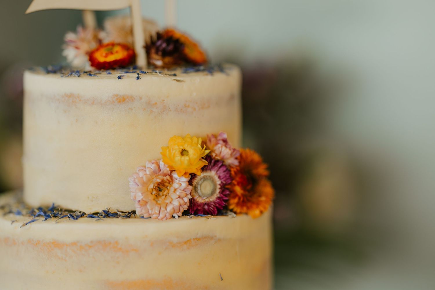 A white wedding cake decorated with fresh autumn-colored flowers and delicate details.