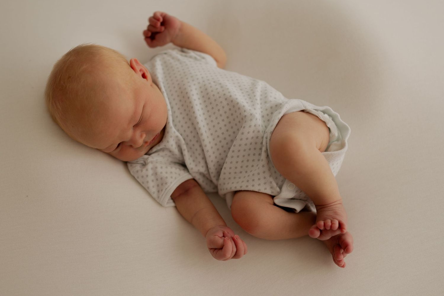 A sleeping newborn baby wearing a polka dot onesie rests peacefully in a series of gentle poses on a beige backdrop.