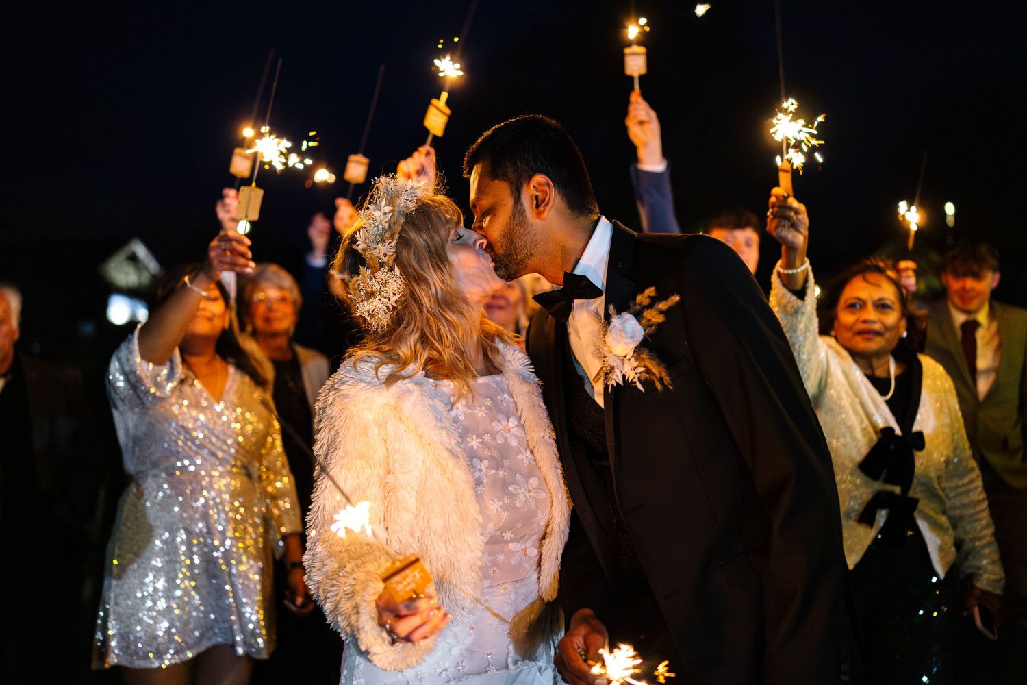 A romantic wedding celebration at night with sparklers glowing as guests surround the couple during their special moment.