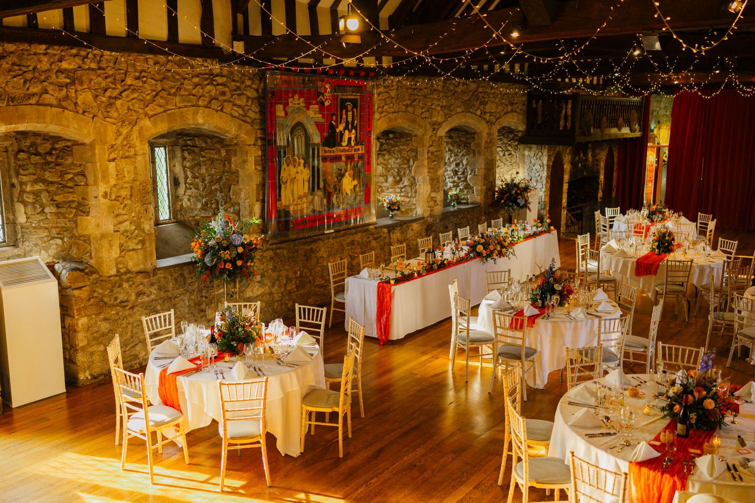 An elegant reception hall with stone walls and wooden beams set for a wedding celebration.