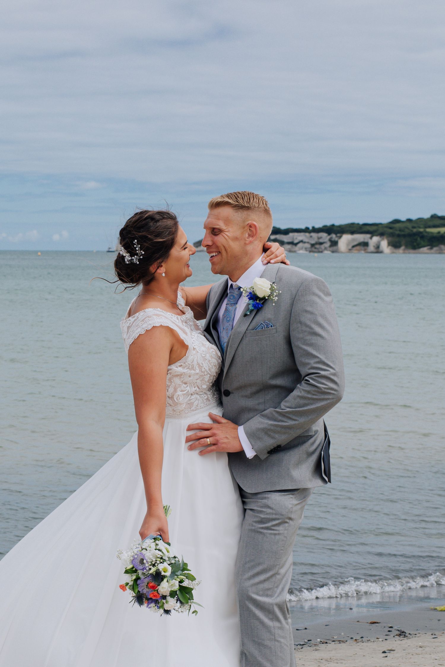 Newlyweds share intimate moment on beach with ocean backdrop.