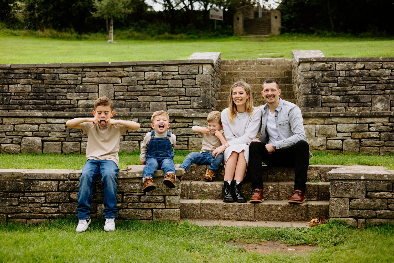 Happy family posing on stone steps in a green park setting.