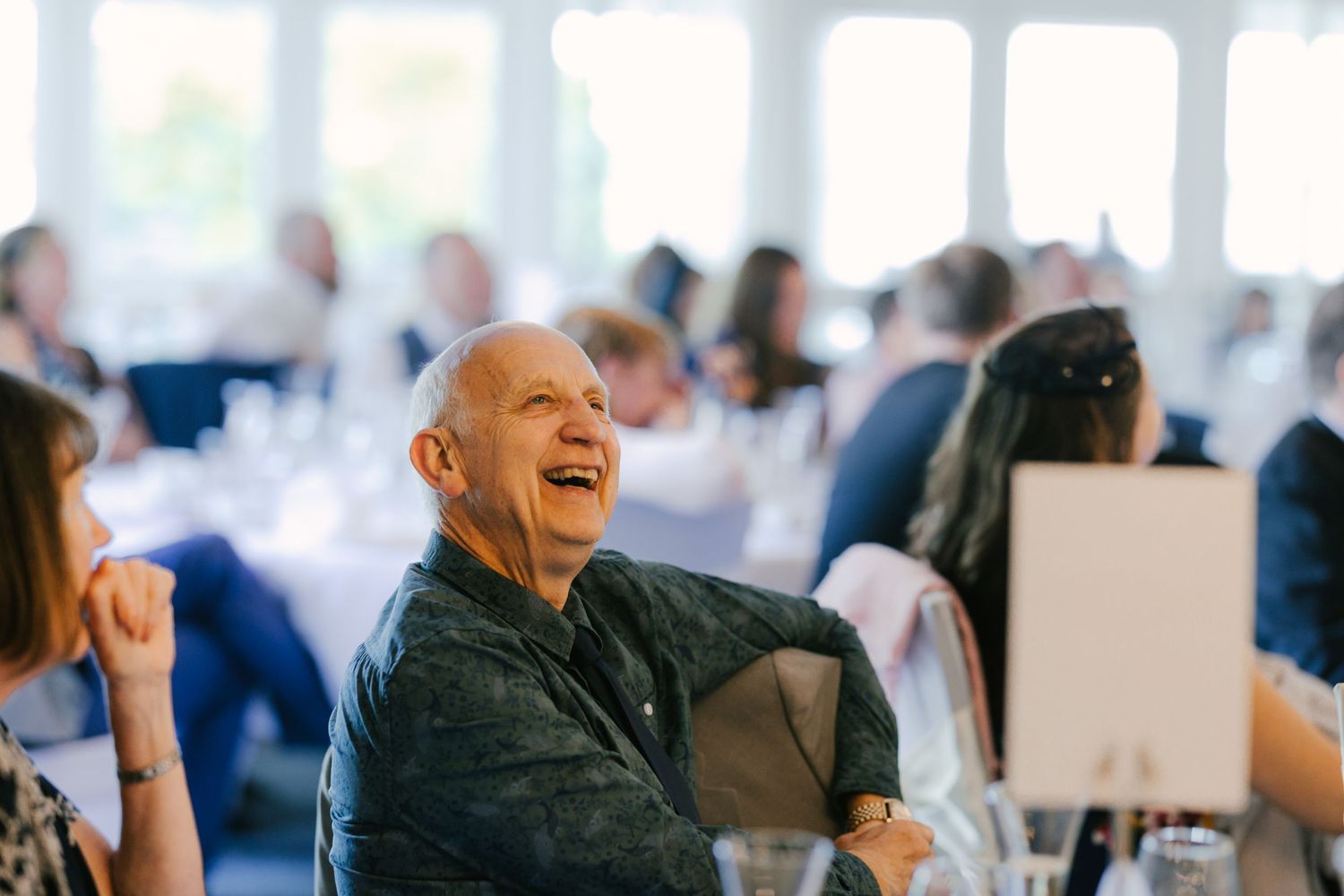 A guest laughing heartily during a wedding reception in a bright banquet hall.
