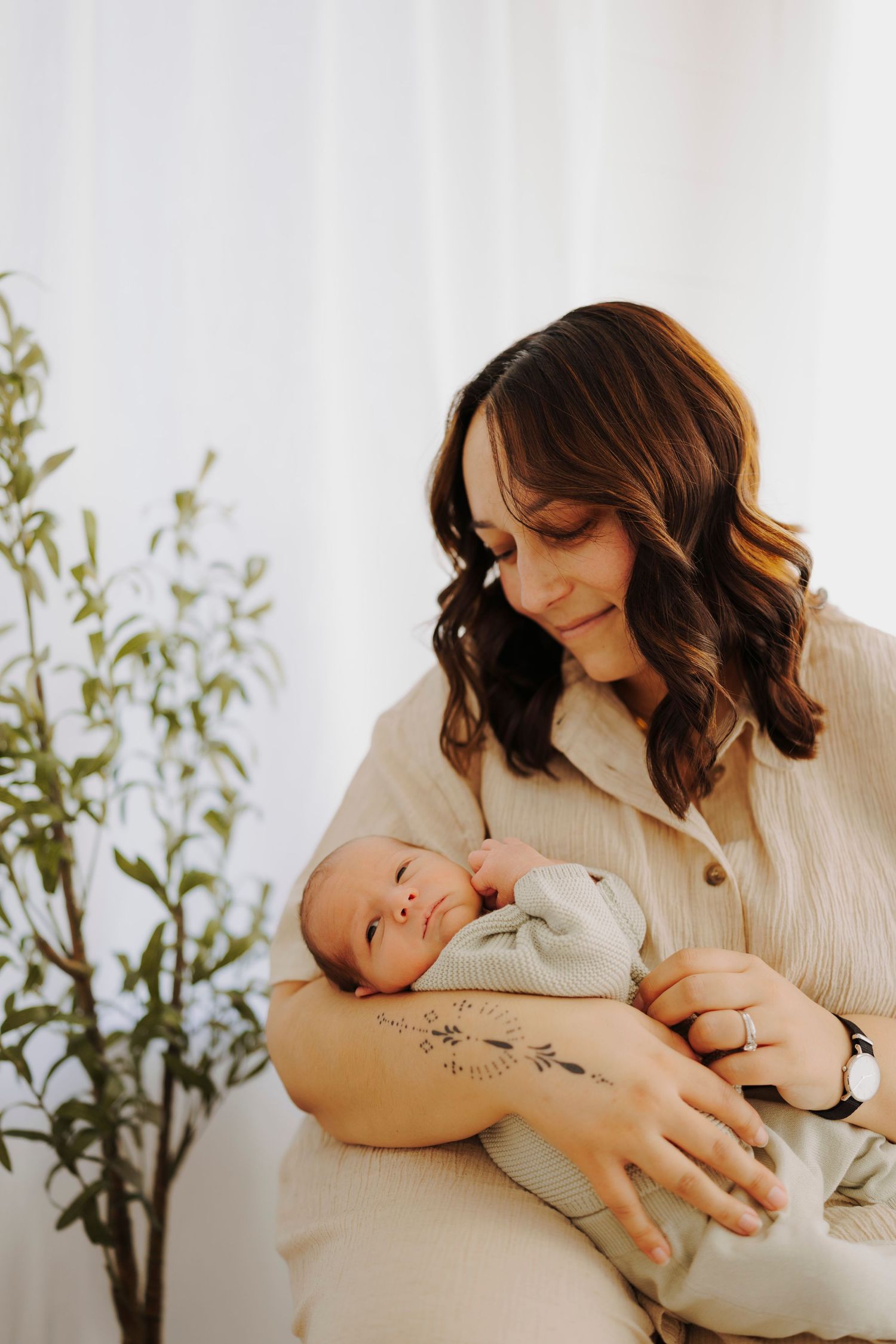 Mother in cream colored shirt holding and gazing at her newborn baby.