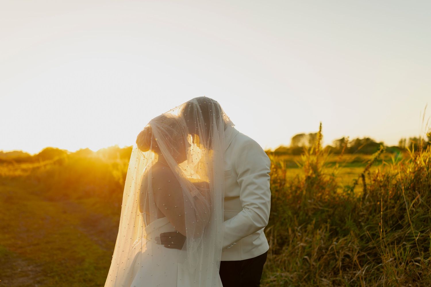 A couple shares a romantic moment at sunset in a field with golden light streaming through their silhouettes.