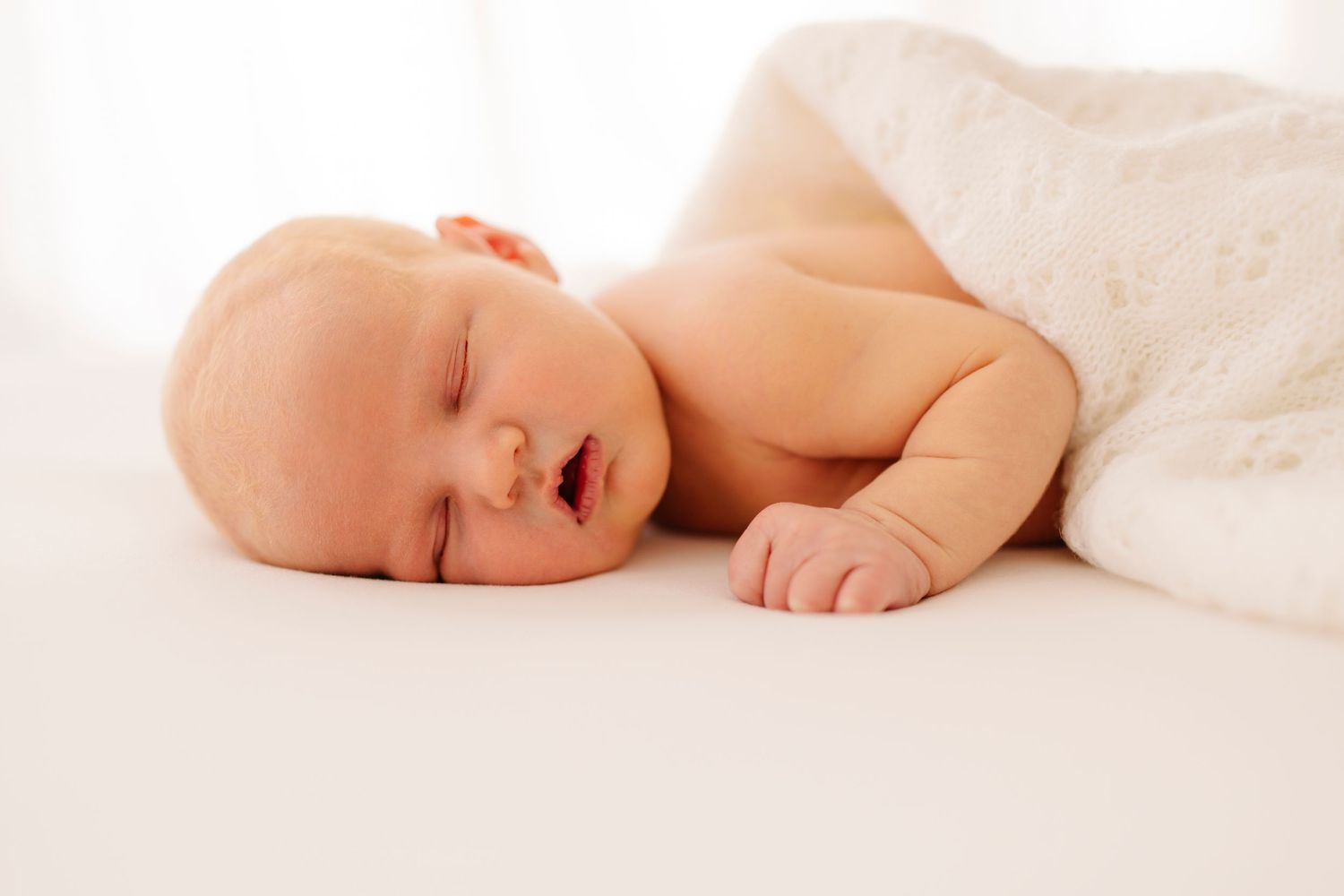 Peaceful sleeping baby wrapped in soft white blanket on white background.