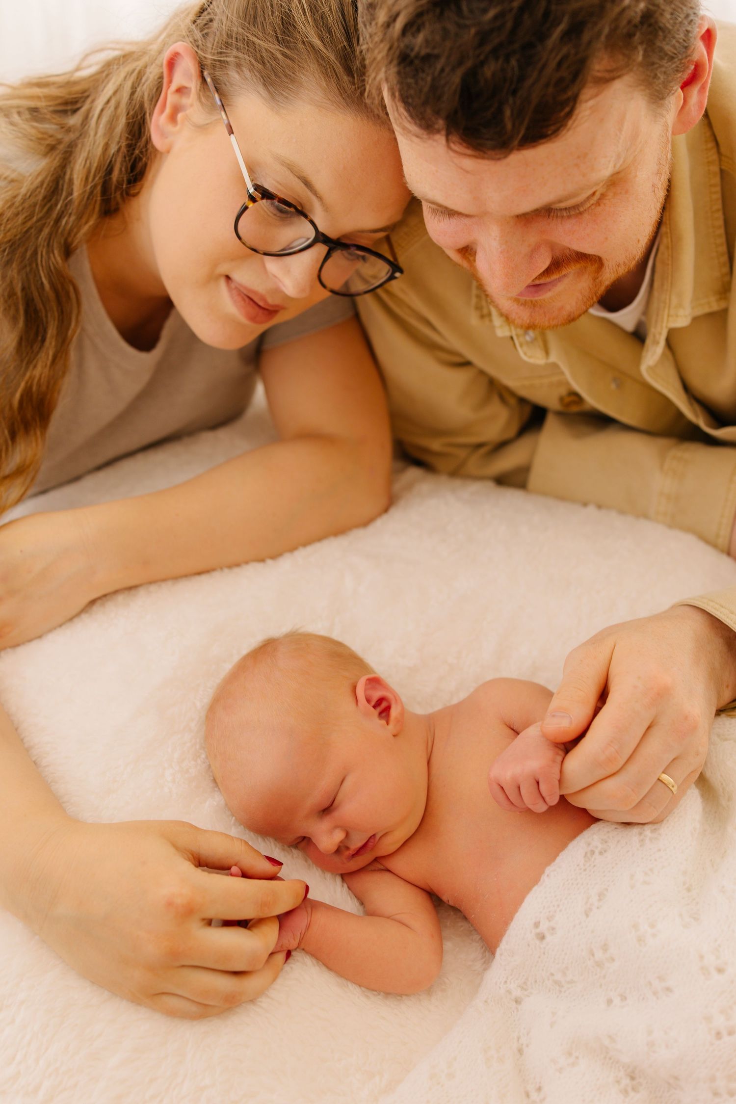 Sweet moment of new parents gazing at their sleeping newborn on white blanket.