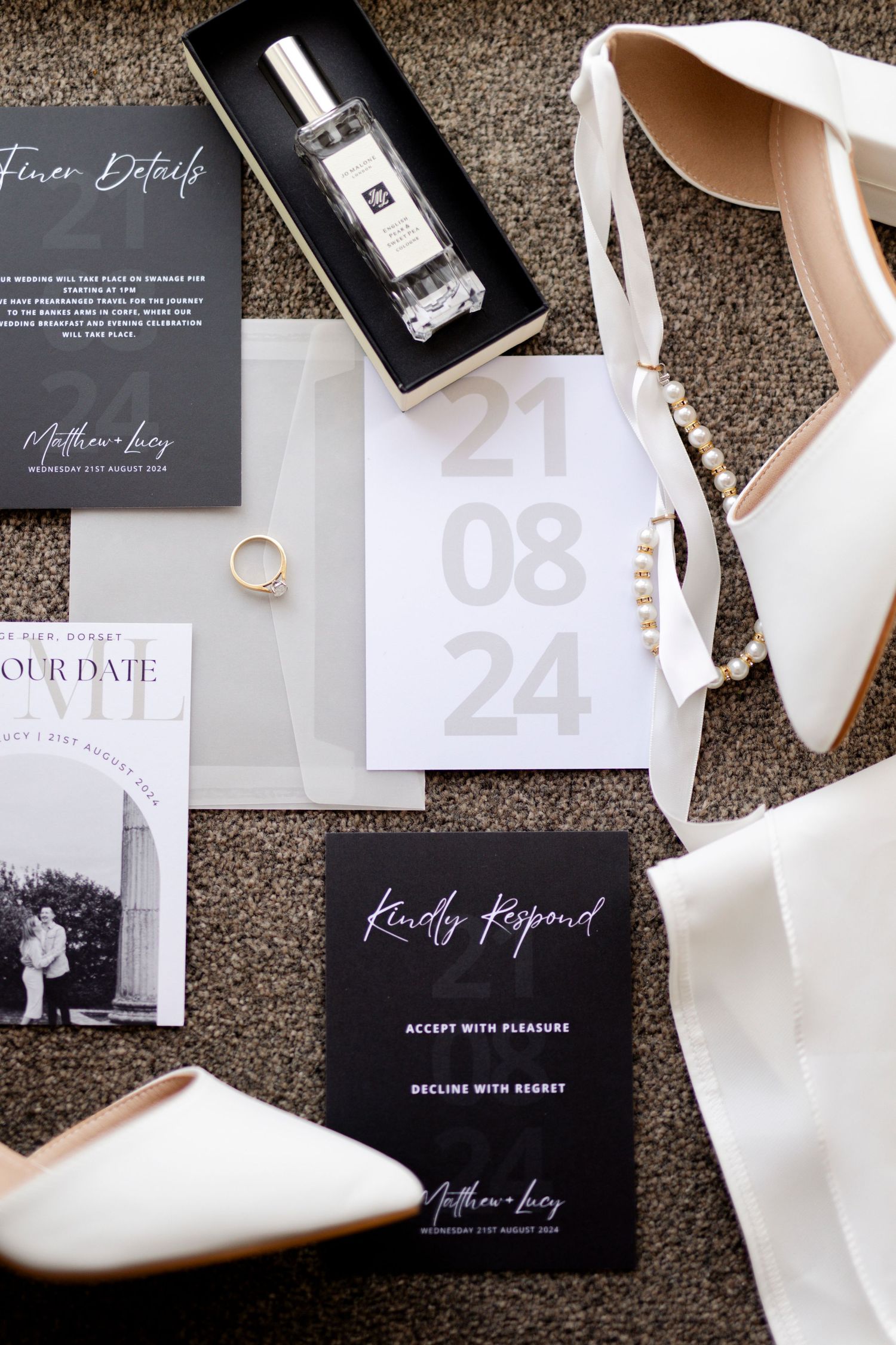 Wedding details flatlay with invitations, perfume, white shoes, and wedding date card on carpet.