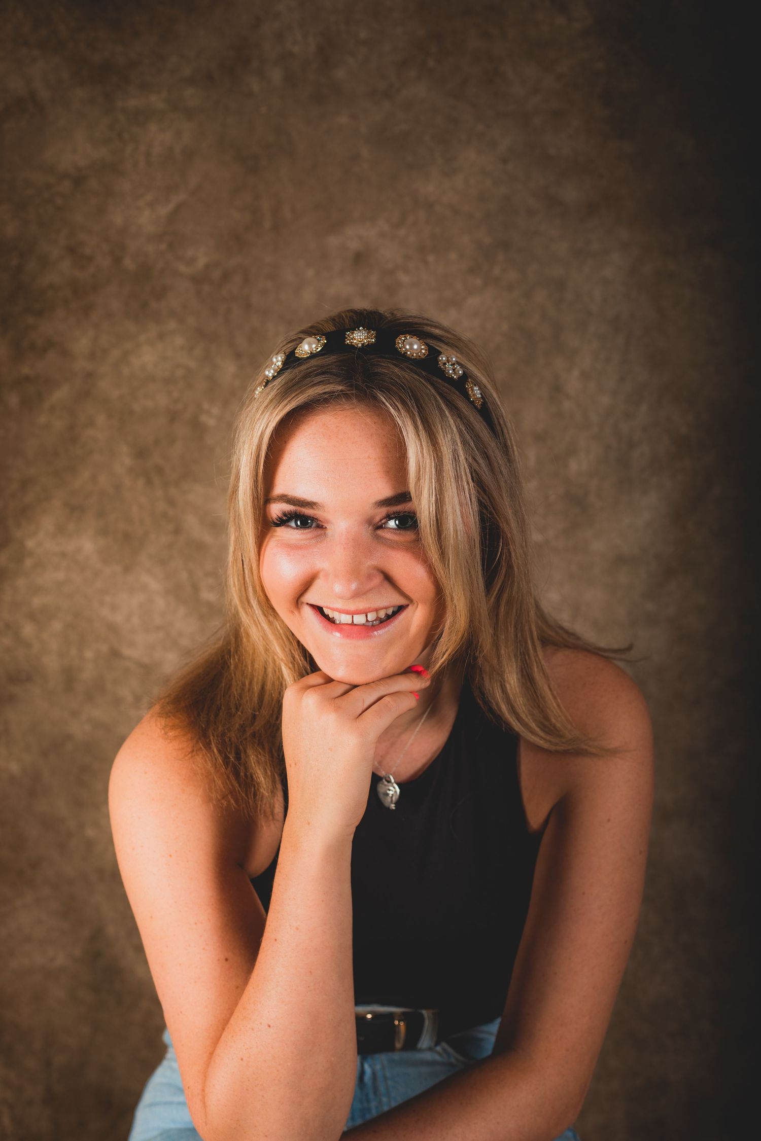Portrait with headband and black top against brown backdrop.