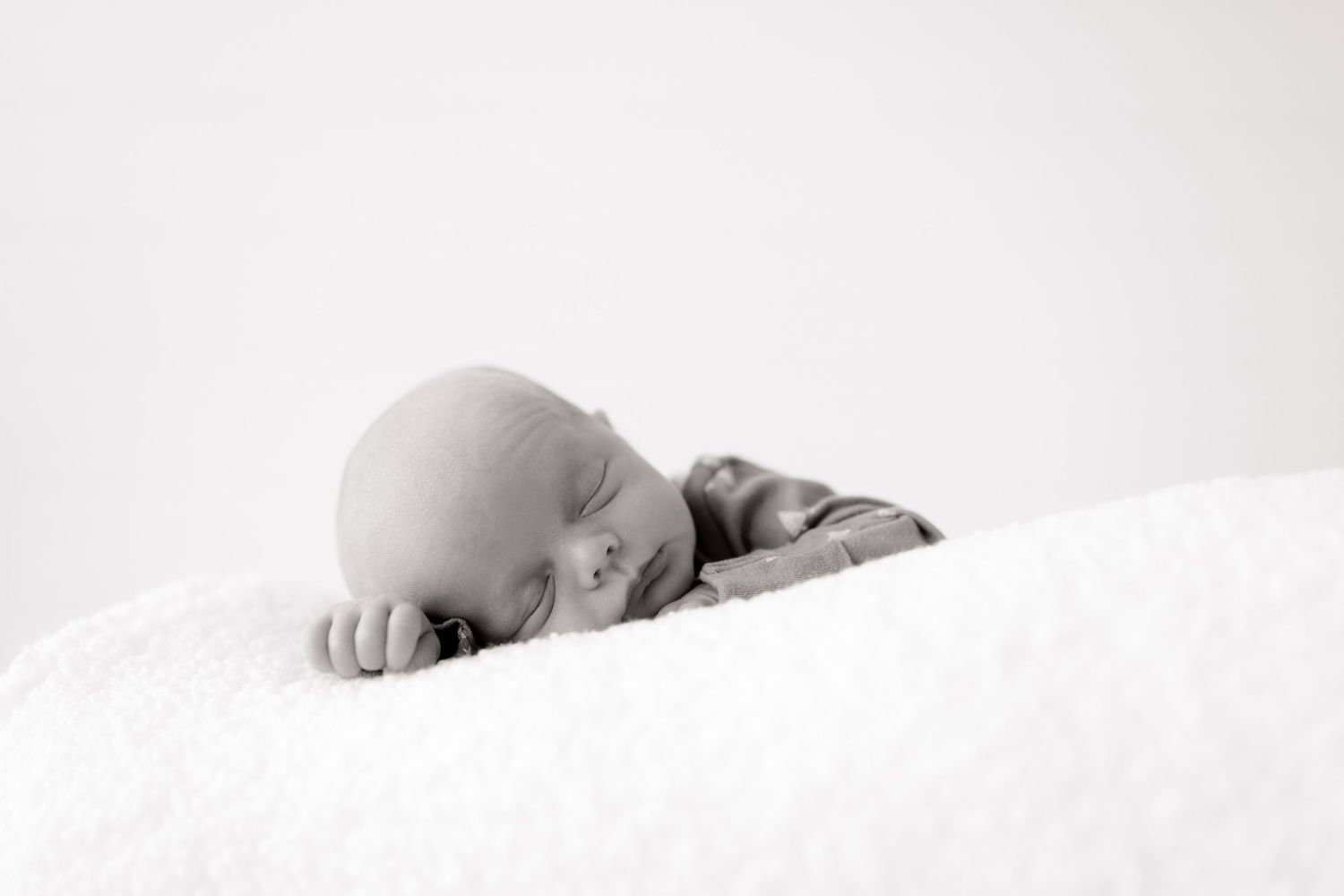 Minimalist black and white photo series showing a sleeping baby in soft white bedding from different angles.