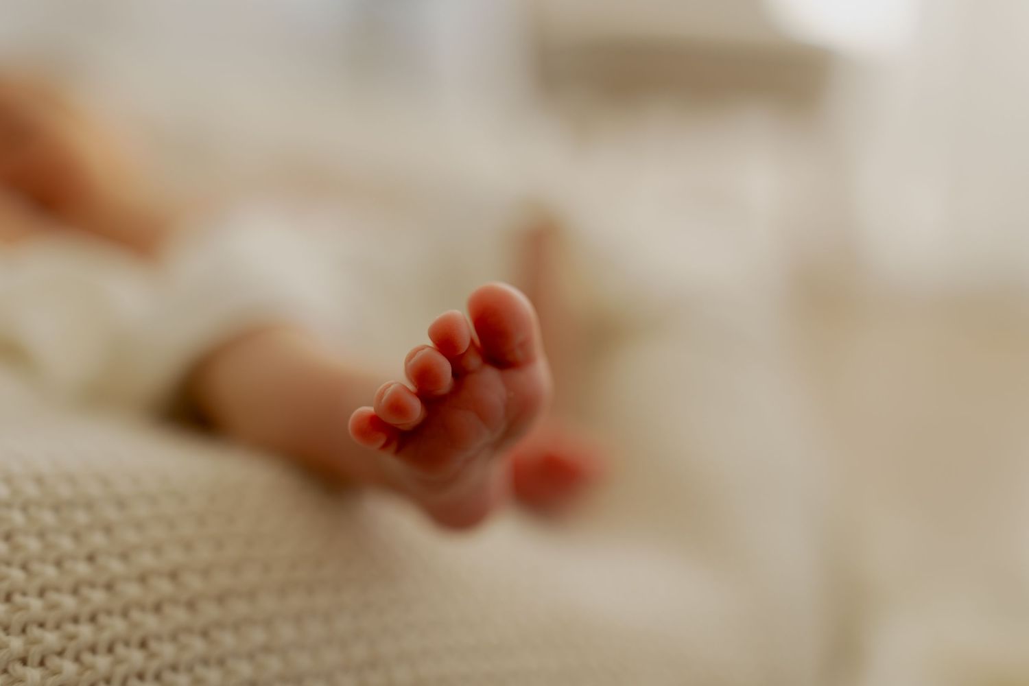 A close-up view of baby feet with tiny toes against a soft beige background.