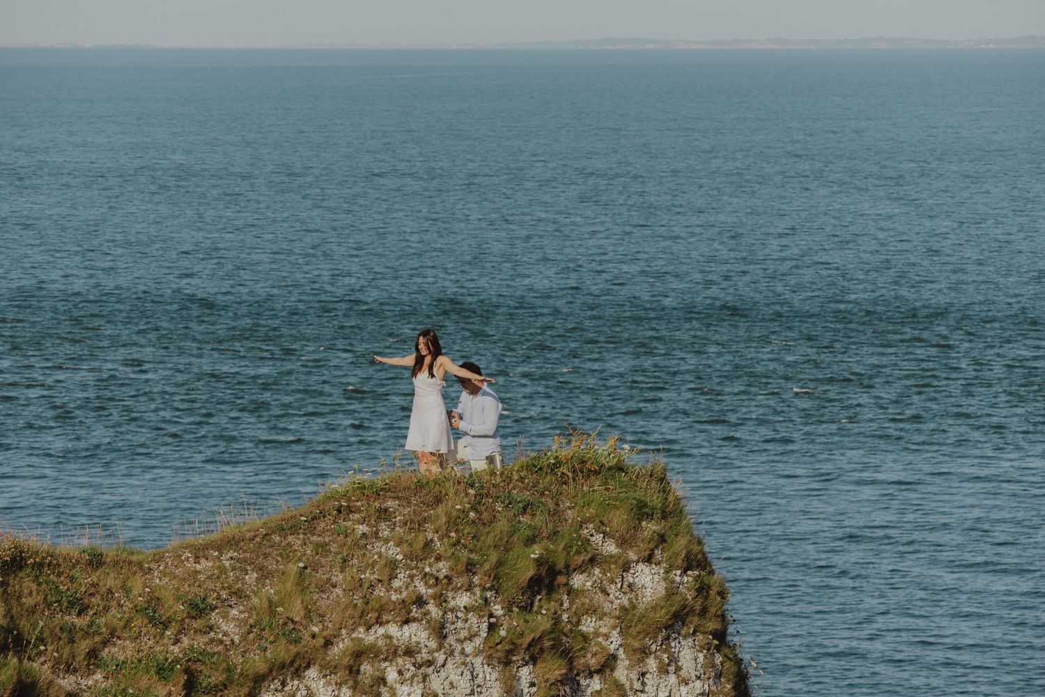 Couple celebrating engagement moment on dramatic oceanside cliff.