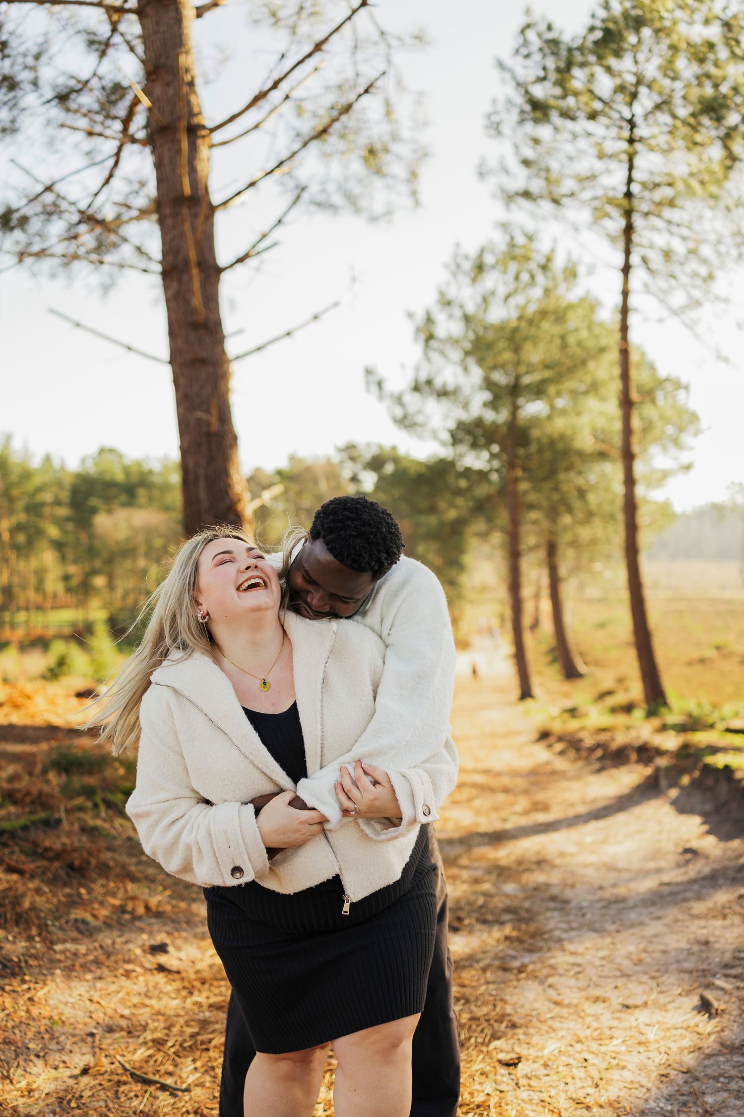 Happy couple laughing and embracing on a sunlit forest trail.