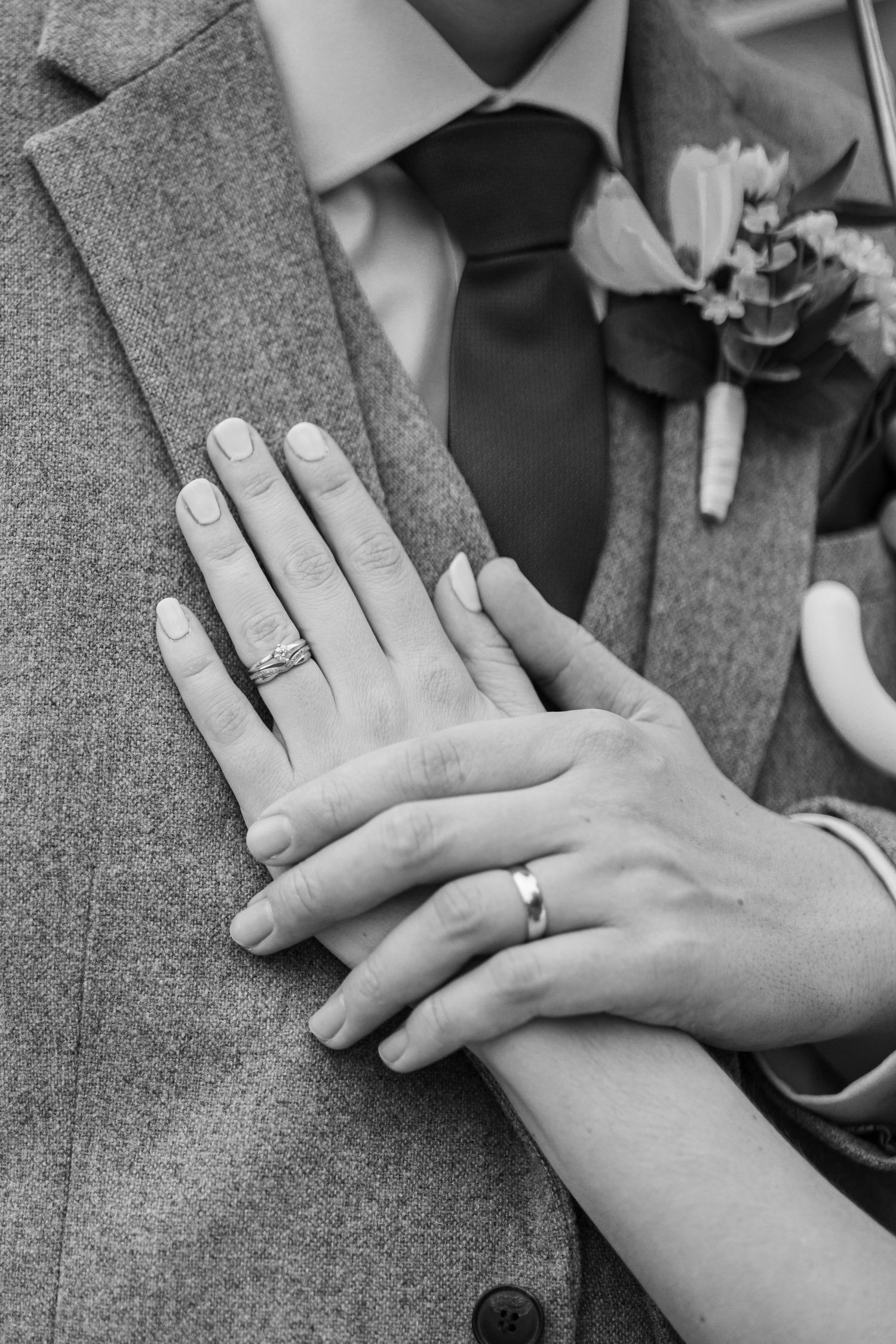 Close-up of wedding rings and hands resting on a gray suit jacket.