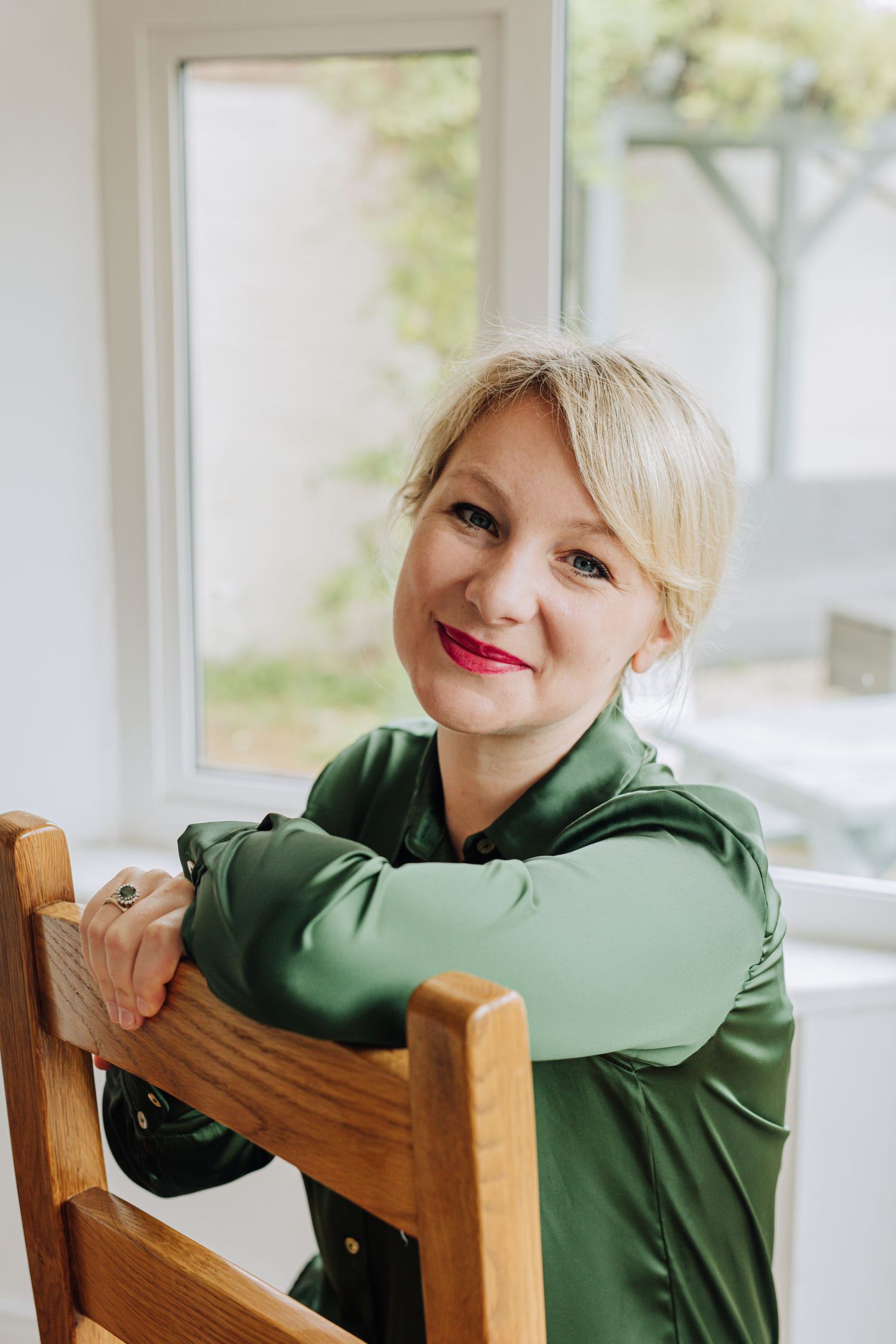 Person in green hoodie rests on wooden chair by window.