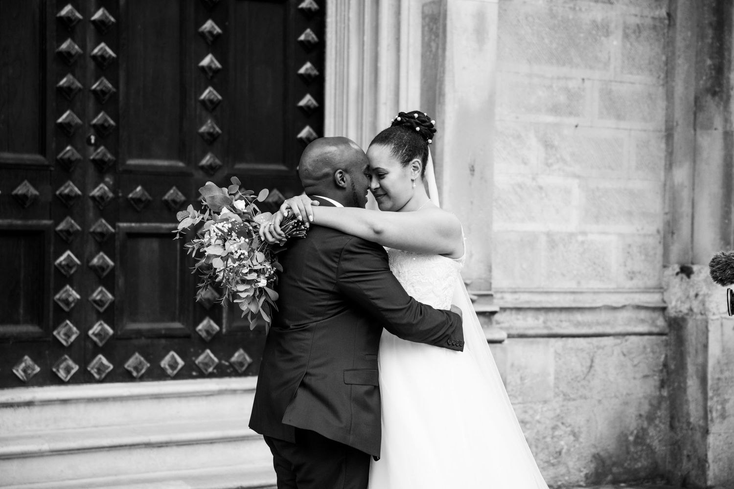 A tender embrace captured in black and white outside a historic church building.