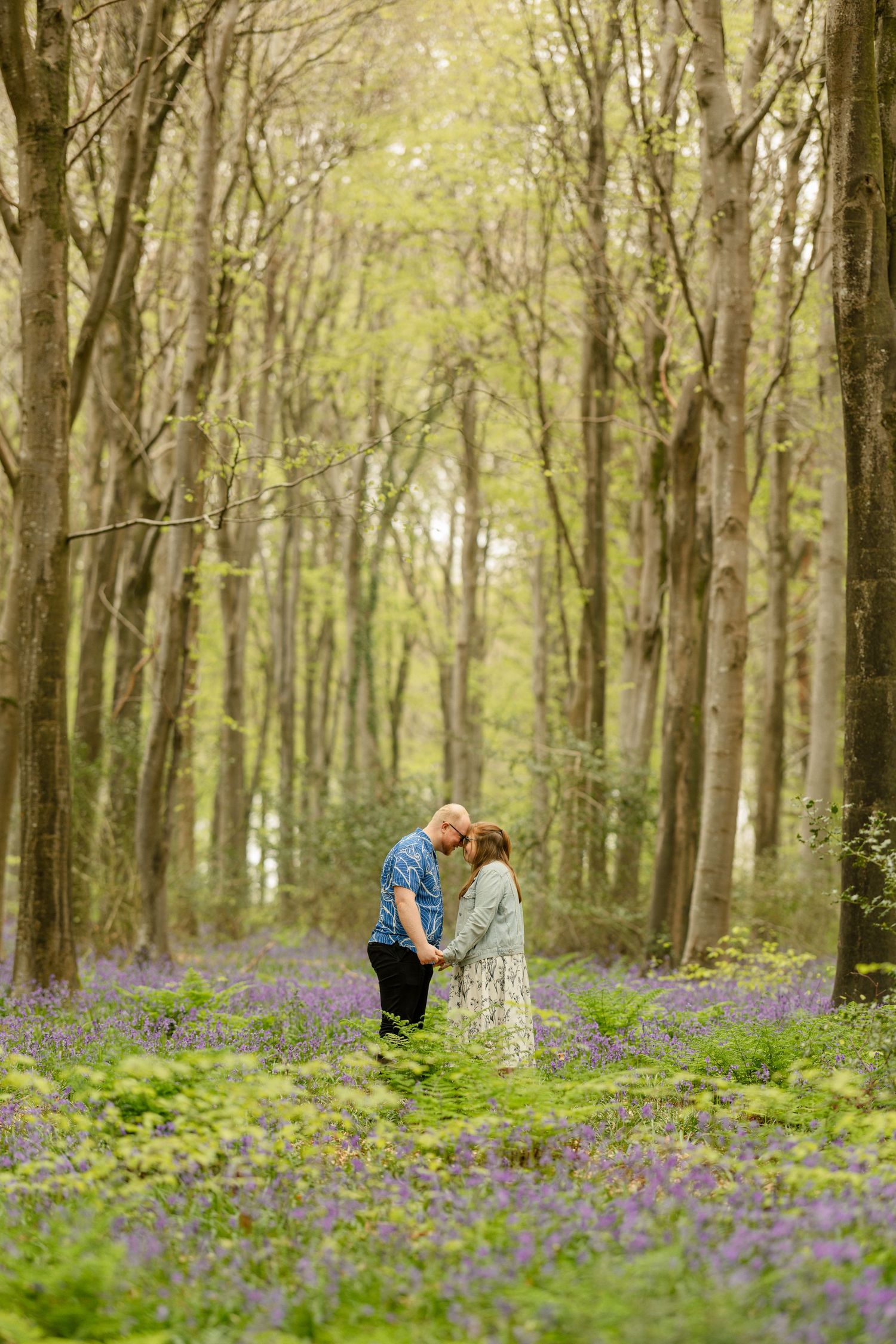 Two people share an intimate moment surrounded by blooming purple wildflowers in a forest.